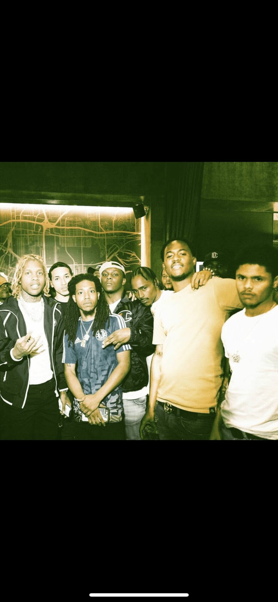 Group of seven people standing together in a dimly lit environment with green lighting, some smiling and looking at the camera.