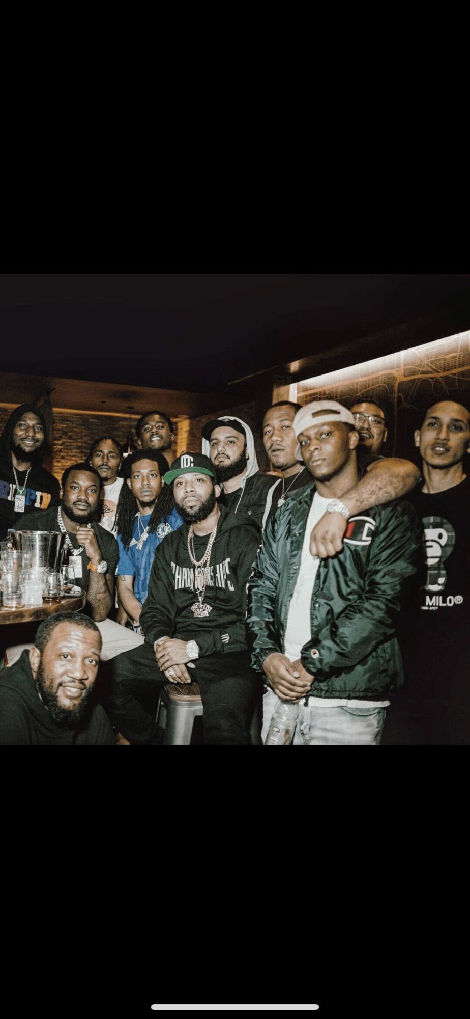 Group of people gathered indoors, some wearing jackets and hats, with a bar or counter in the background.