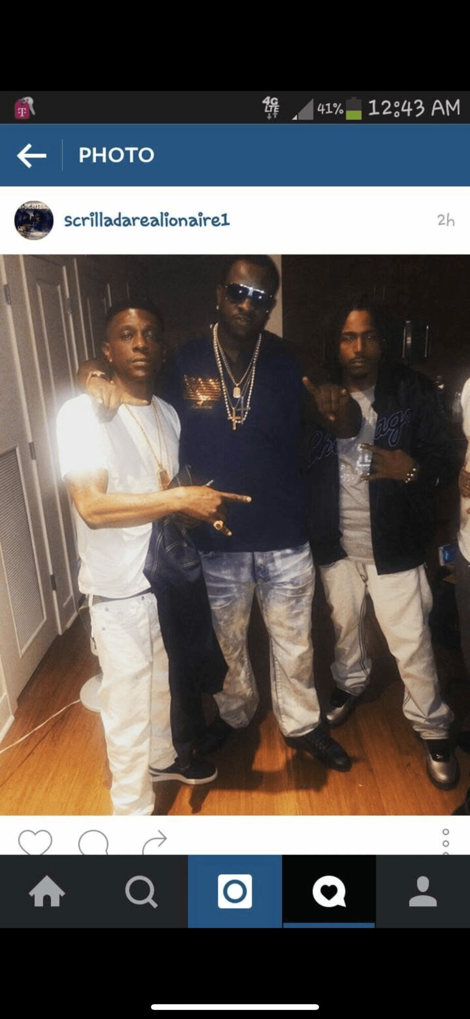 Three men standing indoors, two making peace signs, one wearing sunglasses and jewelry, wooden floor background.