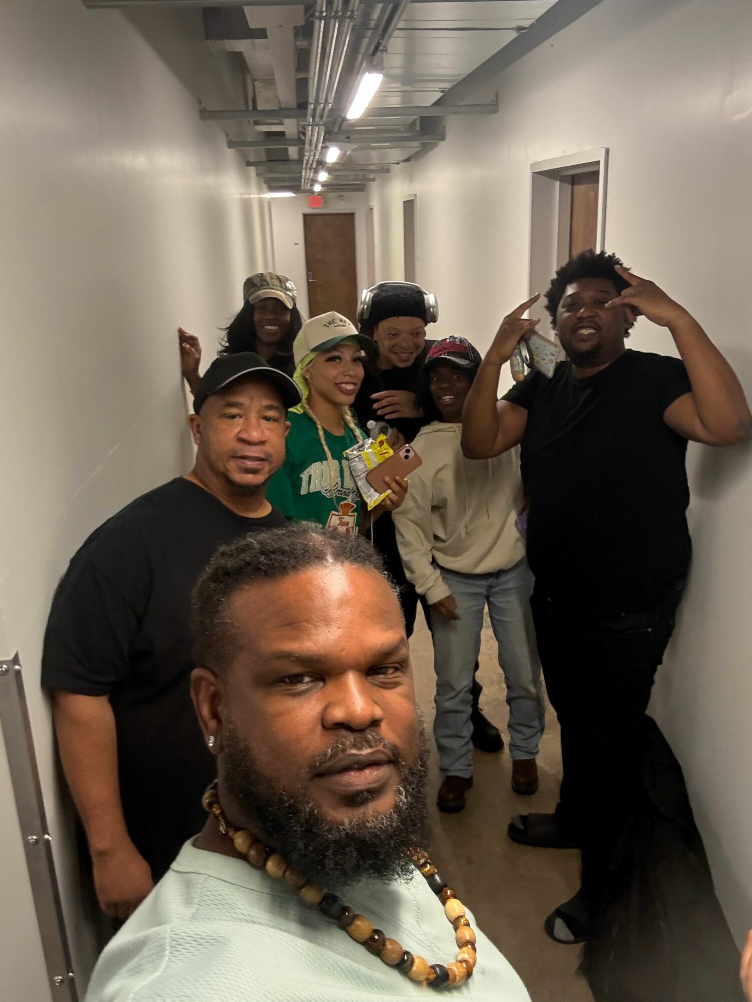 Group of six people in a hallway, some making peace signs, one person taking a selfie, all smiling.