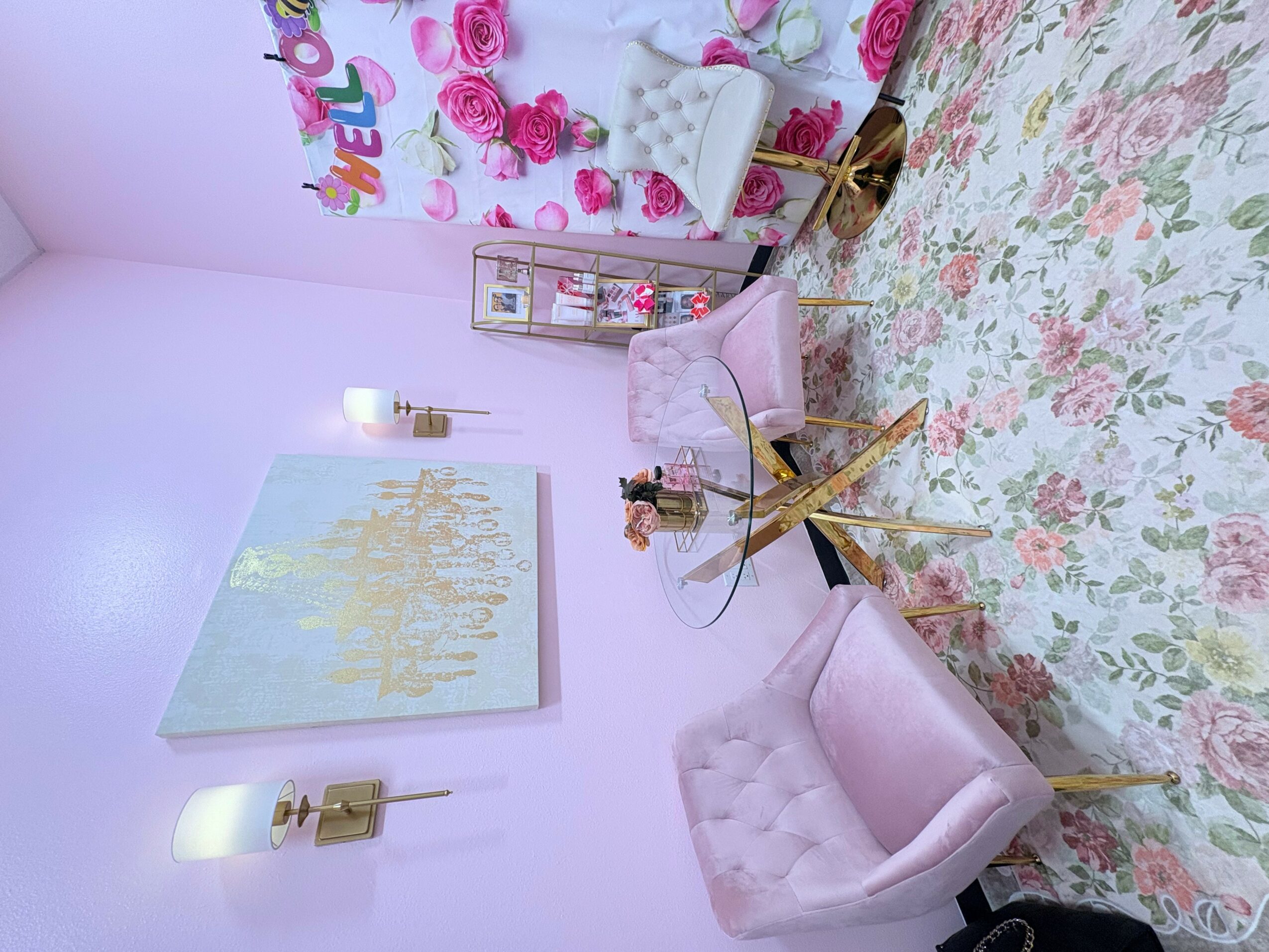 Room with pink walls, floral tablecloth, velvet chairs, and wall art, decorated with roses and a