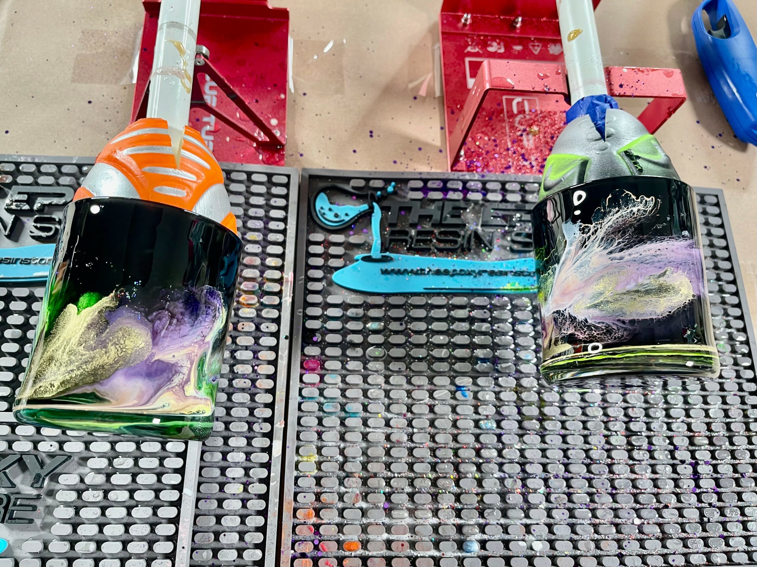 Two fish-shaped objects with colorful designs are placed on a black grid surface, with various tools and containers around them.