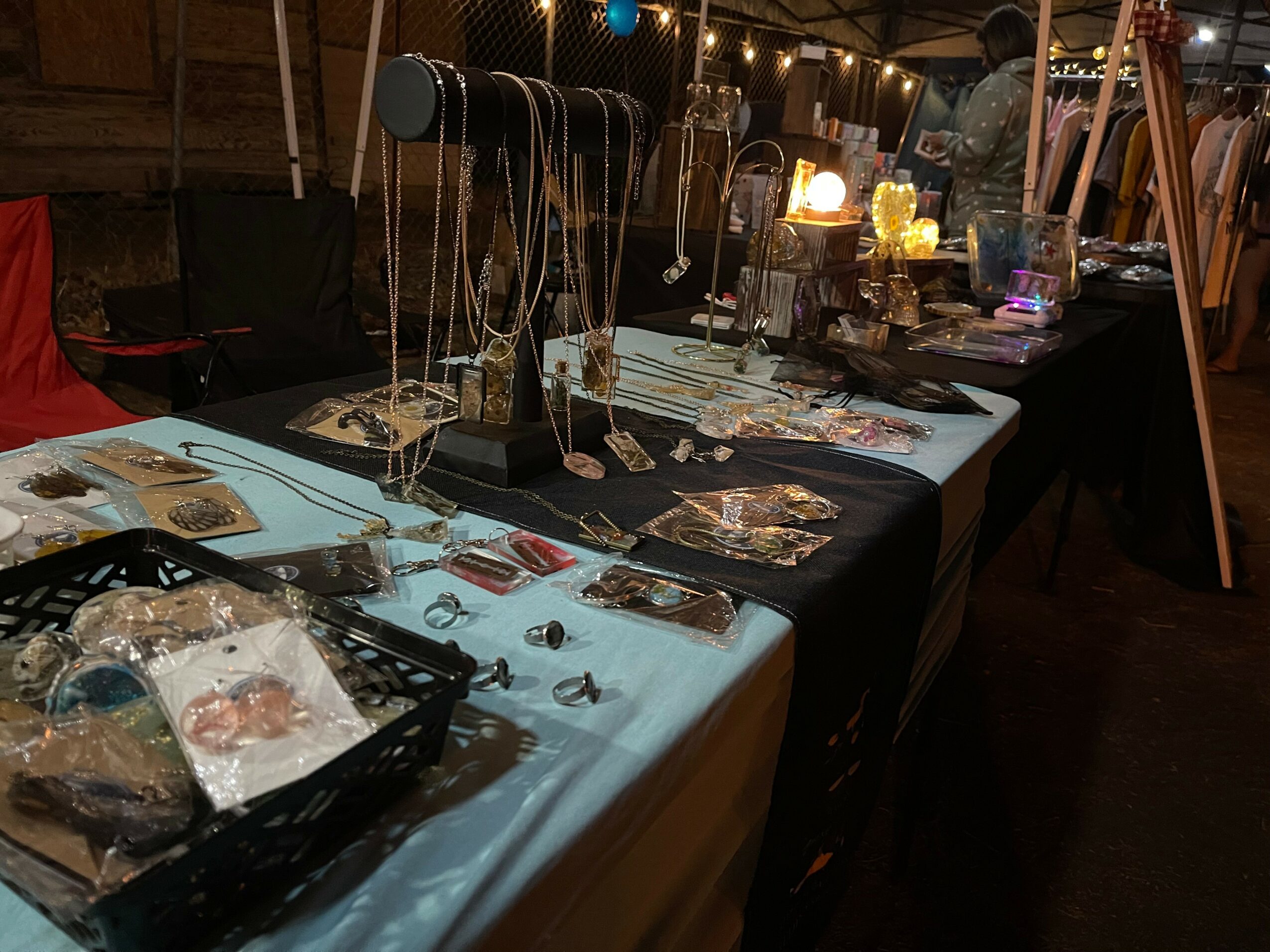 Jewelry display table with necklaces, rings, and earrings at an outdoor market stall, illuminated by warm lighting.
