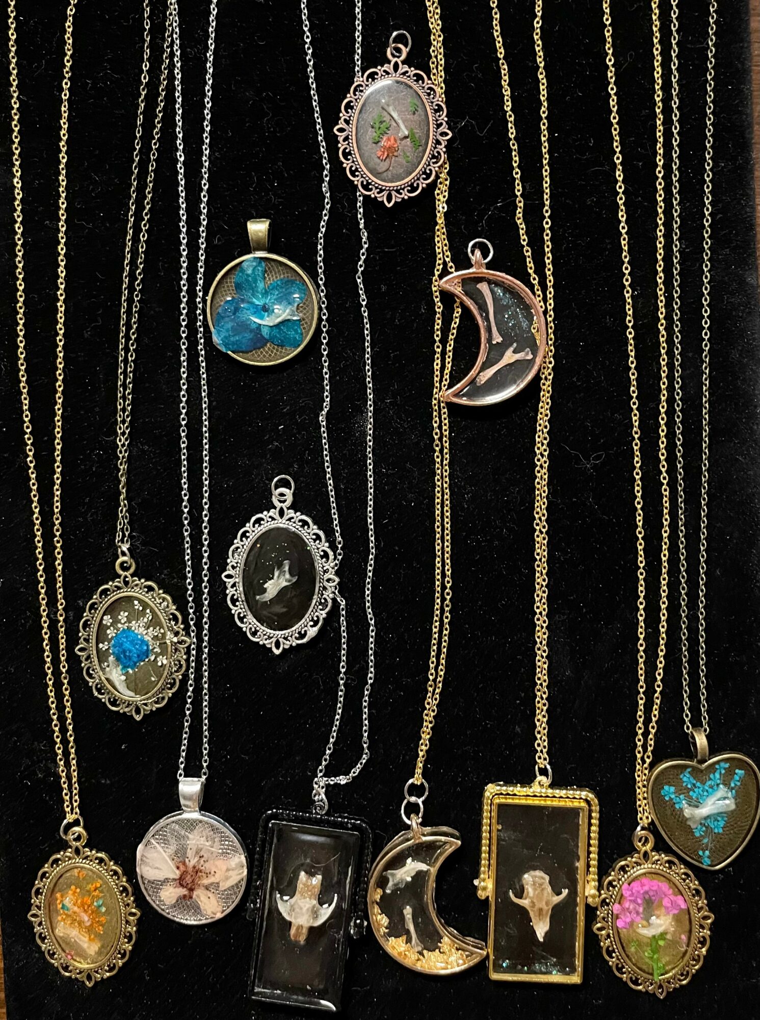 Collection of necklaces with various pendants, including a moon, cat, and floral designs, displayed against a black background.