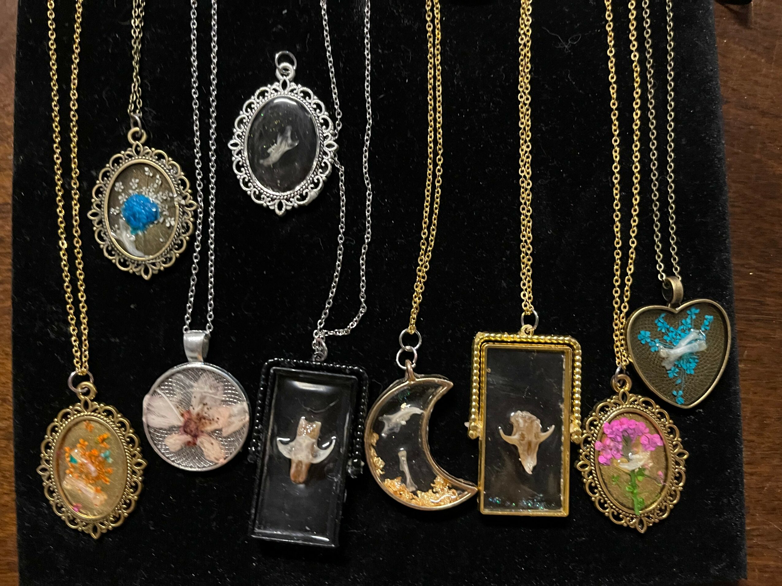 Collection of nine necklaces with various pendants, including animals, moon, and decorative designs, displayed on a black background.