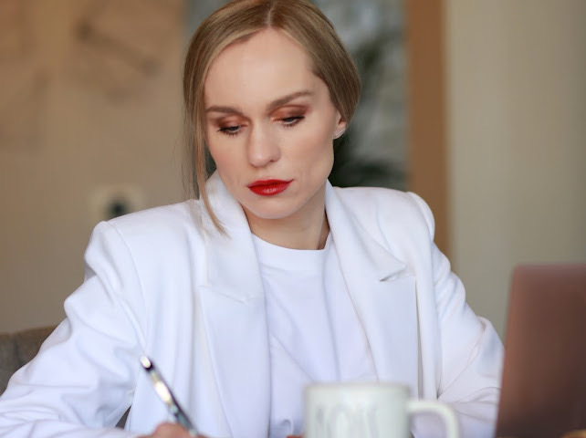 Woman with blonde hair and red lipstick working at a desk with a laptop and mug.