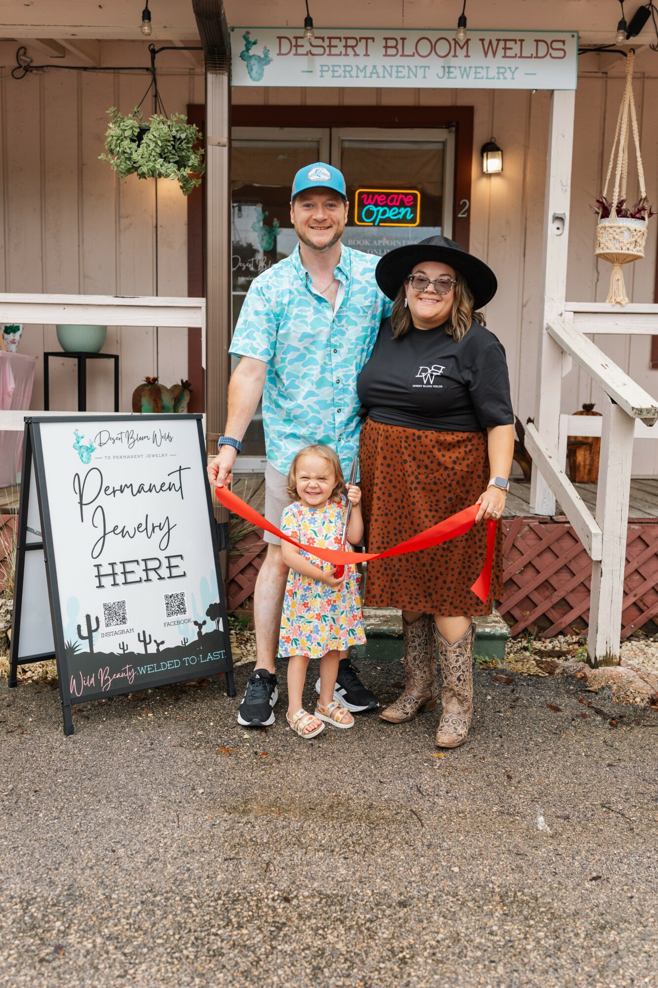 Three people, a man, woman, and child, stand outside a shop with a sign and a ribbon for a grand opening.