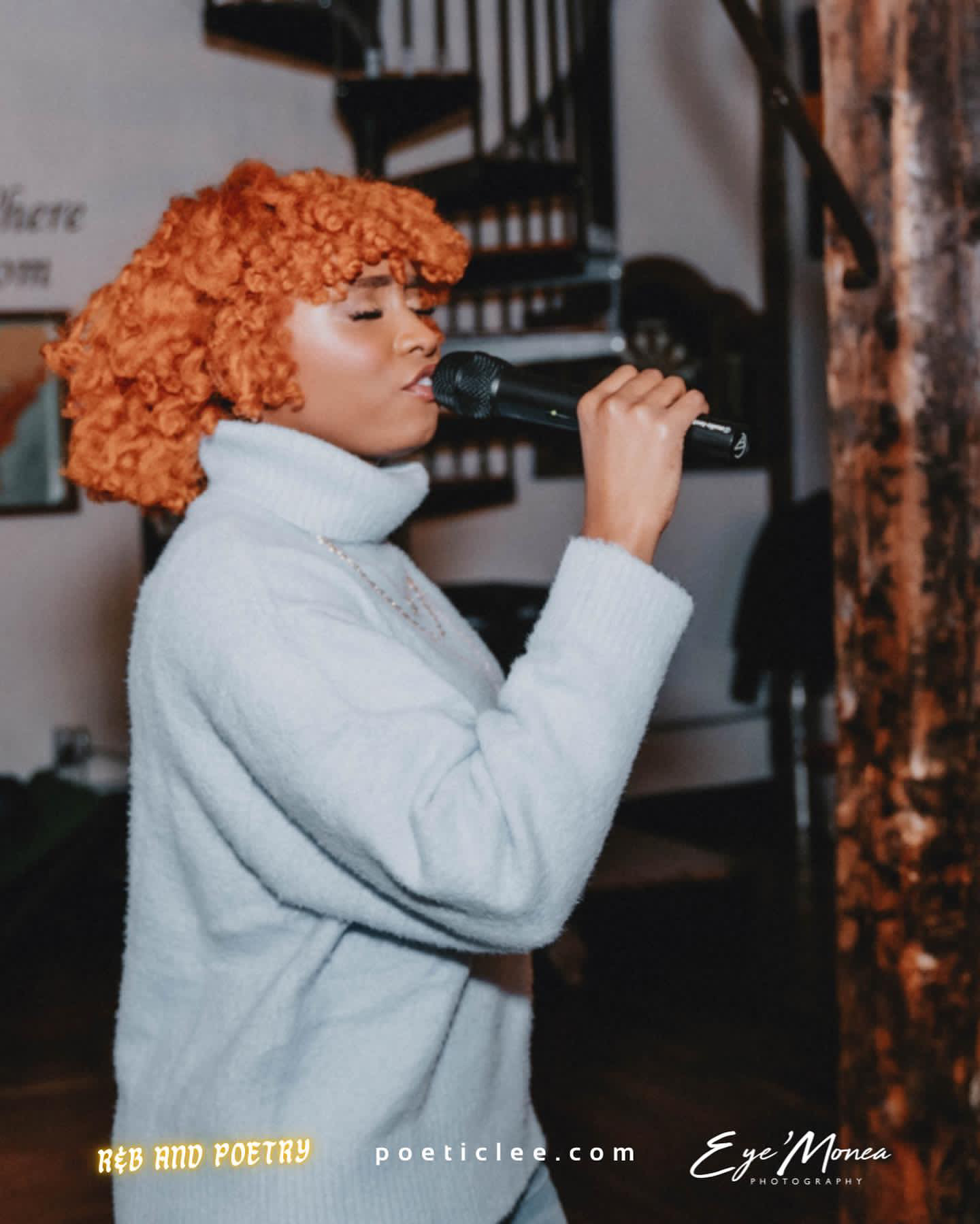 Woman with curly orange hair singing into a microphone indoors, wearing a white turtleneck sweater.