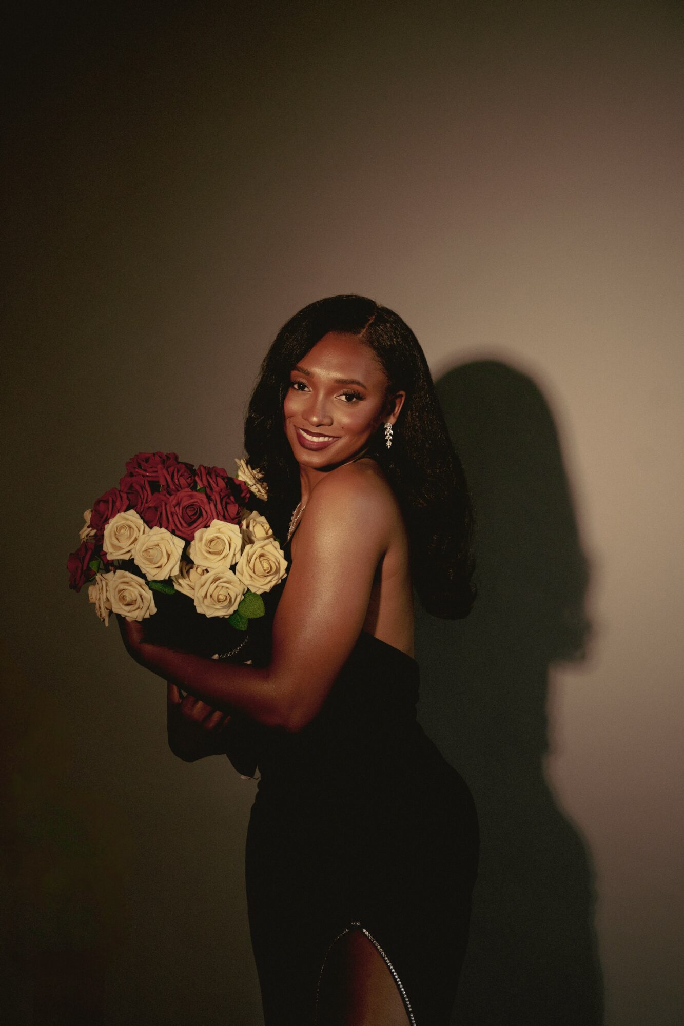 Woman holding a bouquet of red and white roses, smiling, with a shadow on the wall behind her.