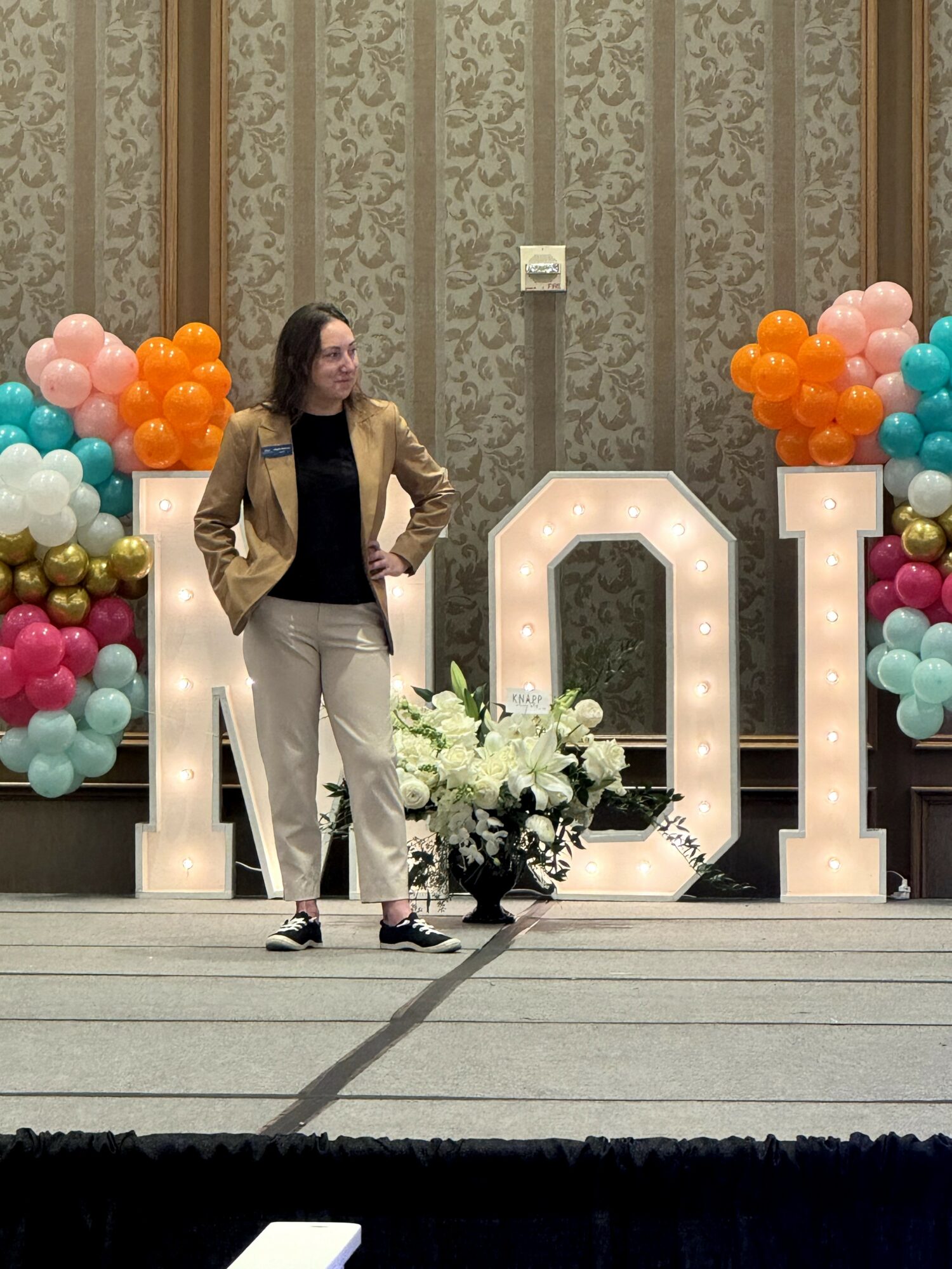 Woman standing on stage with large illuminated numbers and colorful balloon arrangements behind her.