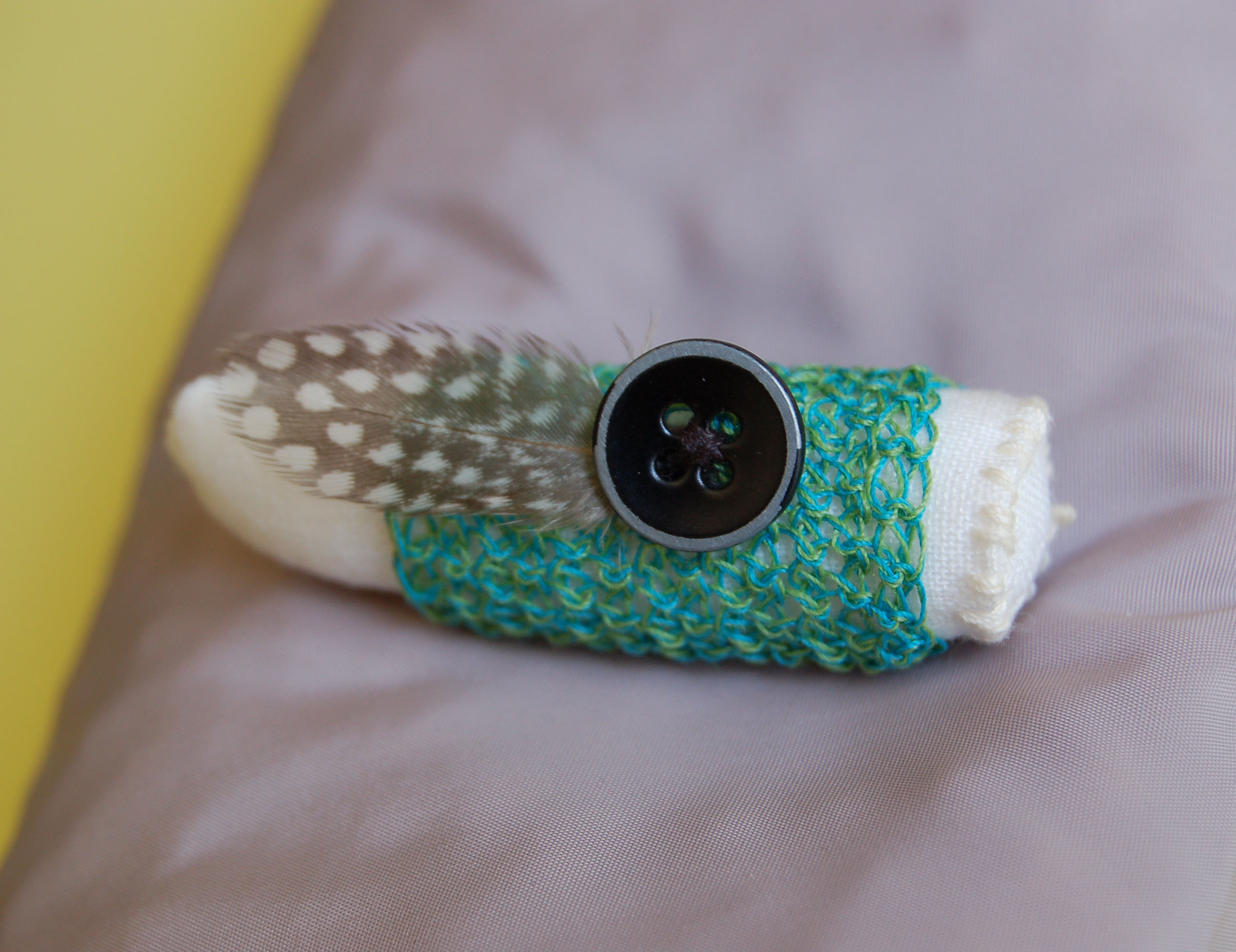 A rolled-up sock with a feather and a button on top, resting on a soft surface.