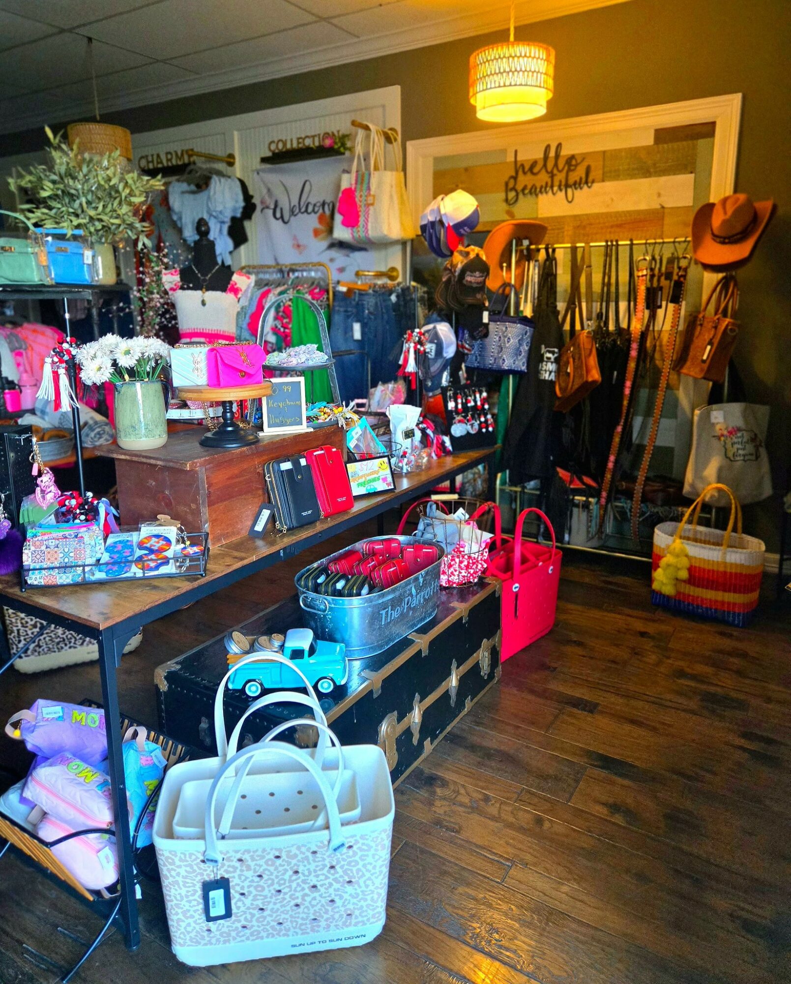 Display of handbags, accessories, and clothing in a boutique store with warm lighting and wooden flooring.