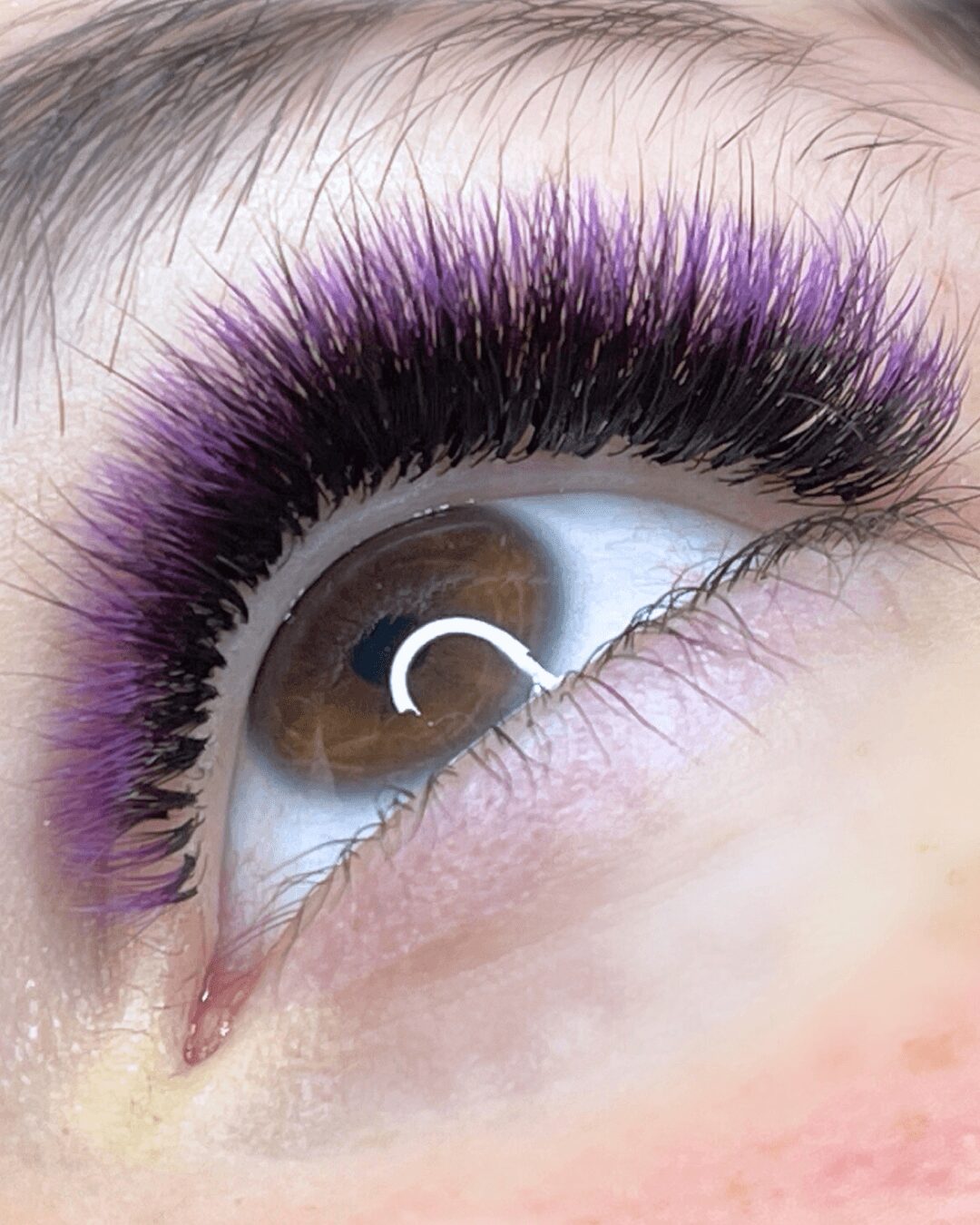 Close-up of a brown eye with long, purple and black eyelash extensions, looking upward.