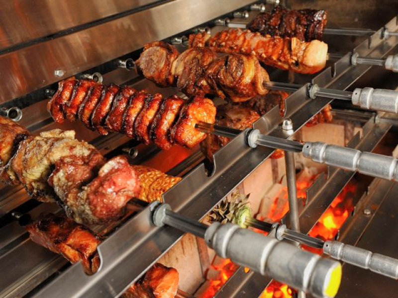 Meat and skewers grilling over open flame on a barbecue, with glowing coals visible below.