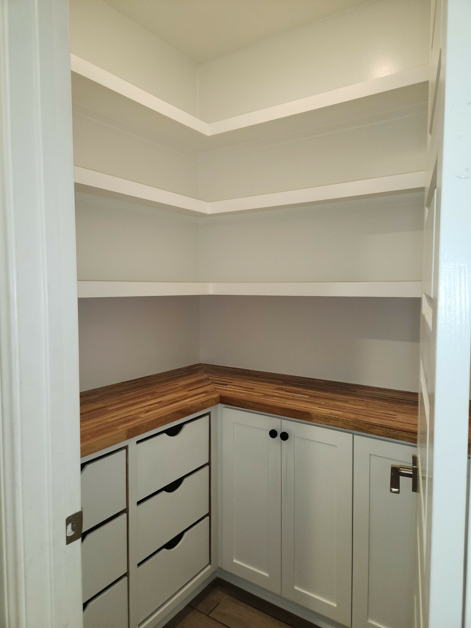 Interior view of a room with white walls, wooden flooring, and a white door with black handles.