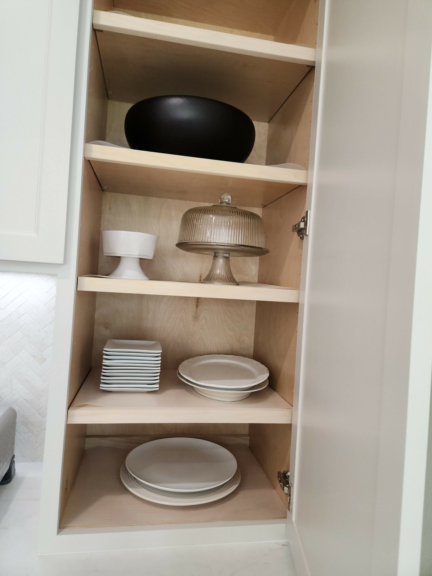 Open drawer with compartments containing black bowl, glass jar, white cup, small plates, and larger plates.
