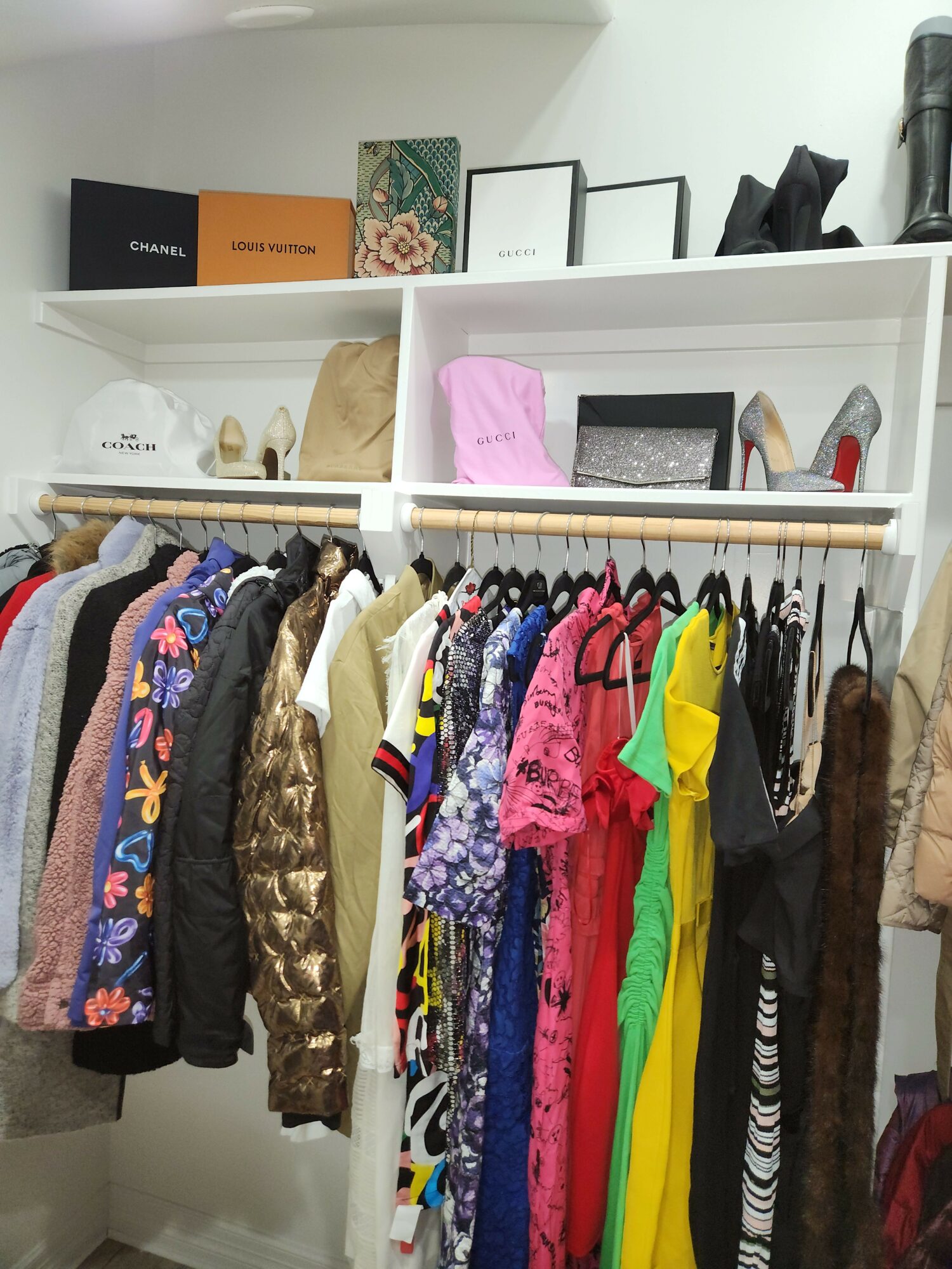 Clothing rack with colorful dresses and skirts, white shelf with boxes and decorative items, and a white wall in the background.