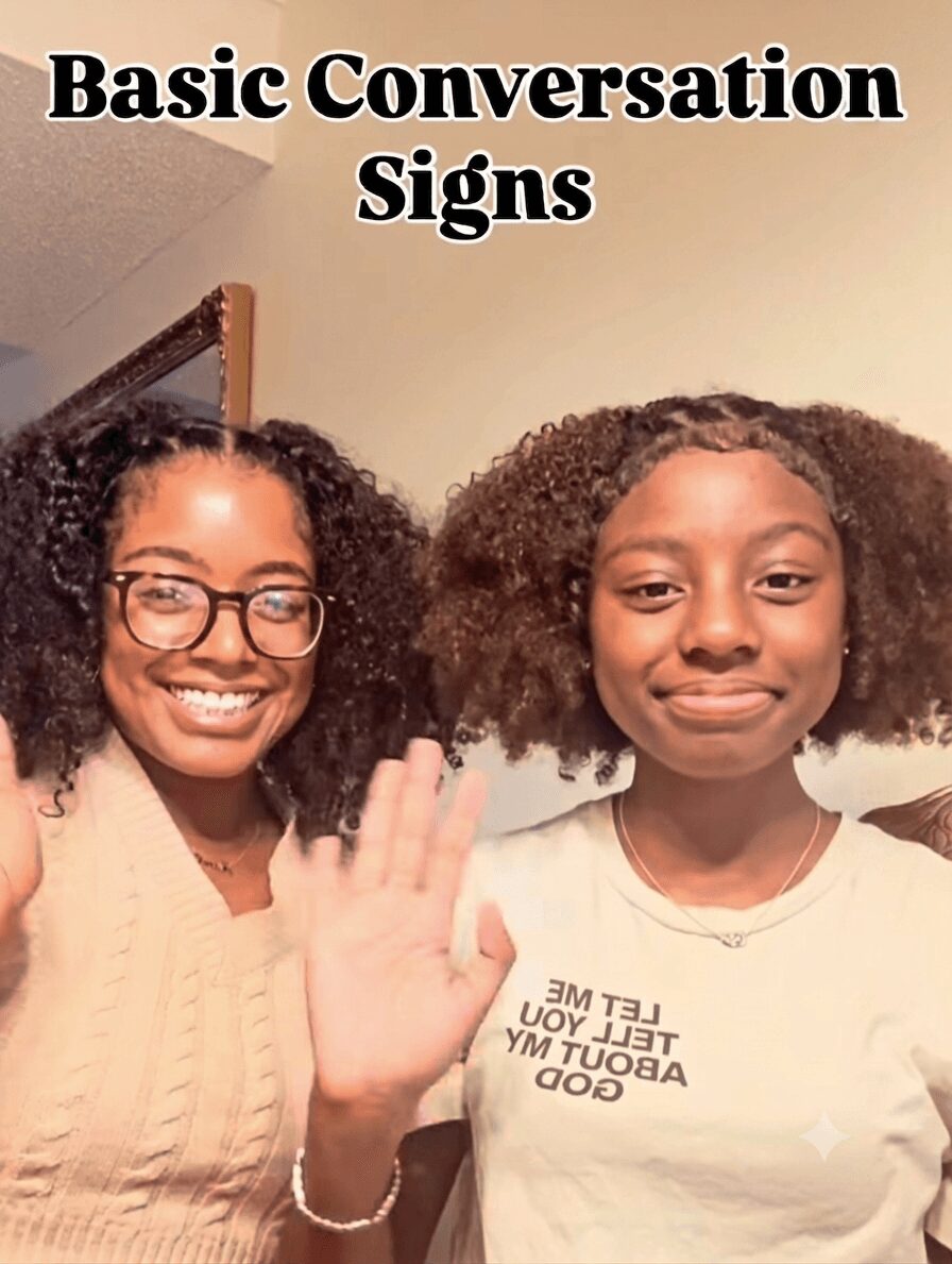 Two smiling young women with curly hair, one waving, standing indoors with a beige wall background.