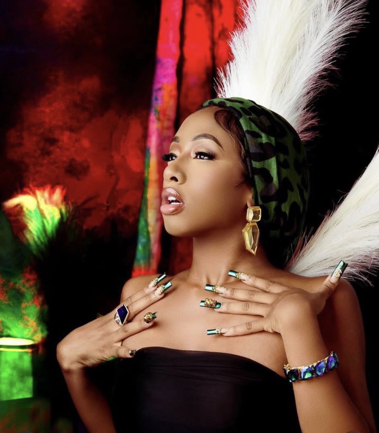 Woman with elaborate headpiece and jewelry poses against colorful background.