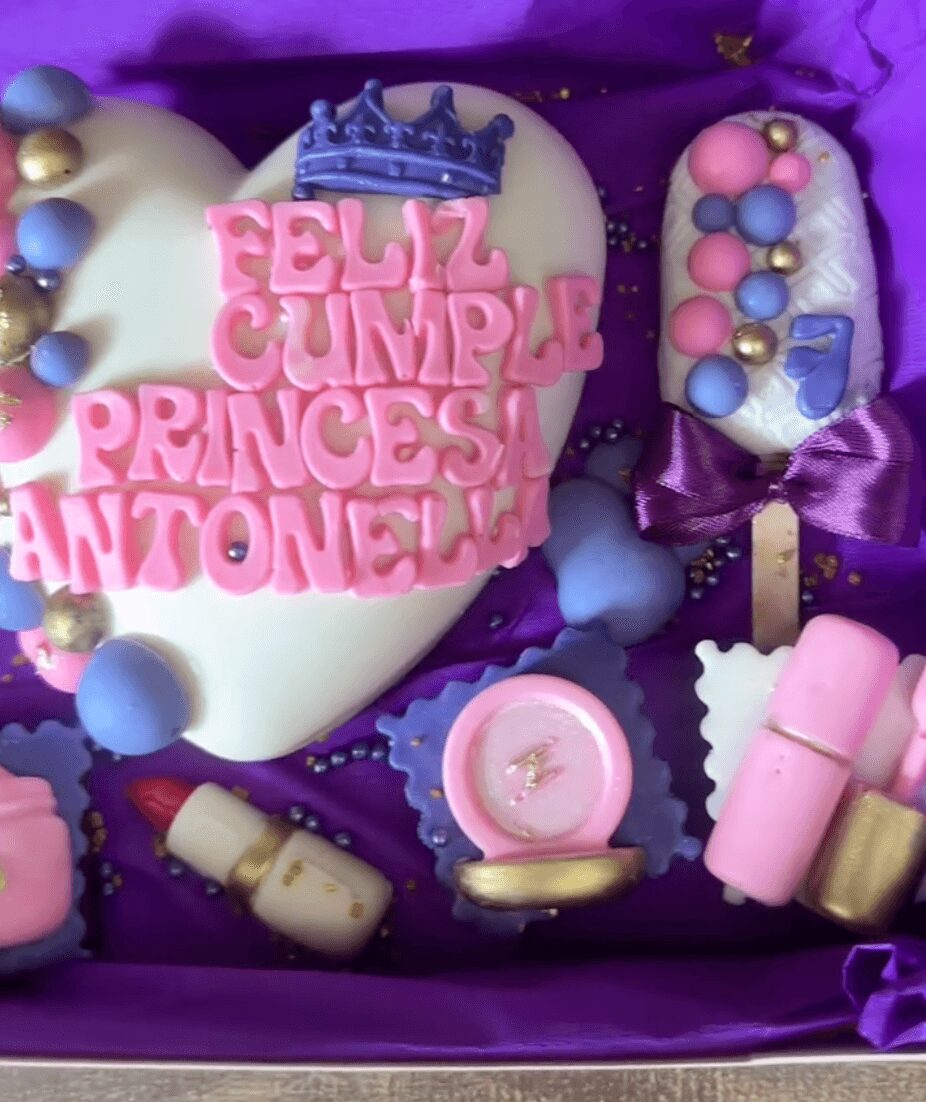 Colorful birthday cake with pink lettering, crown, and various decorated sweets inside a purple box.