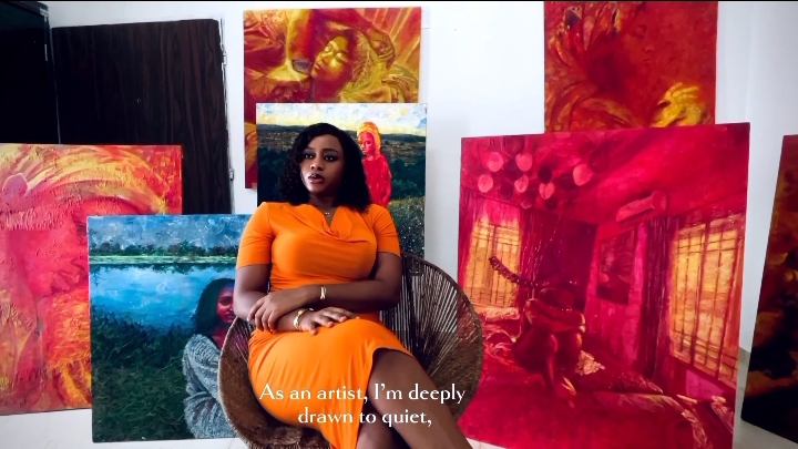 Woman sitting in front of colorful abstract paintings, wearing an orange dress, with a quote about being deeply drawn to quiet.
