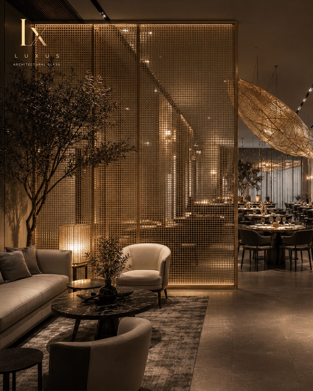 Elegant interior with seating, a tree, and a decorative screen, illuminated by warm lighting, with a dining area in the background.