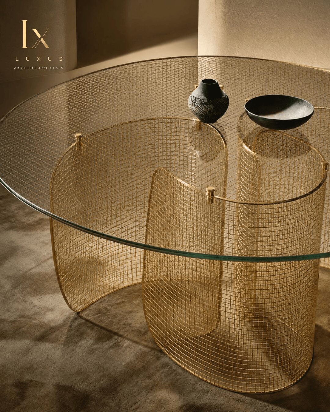 Round glass table with gold wireframe base, two black bowls, and a small textured black vase, in a modern setting.