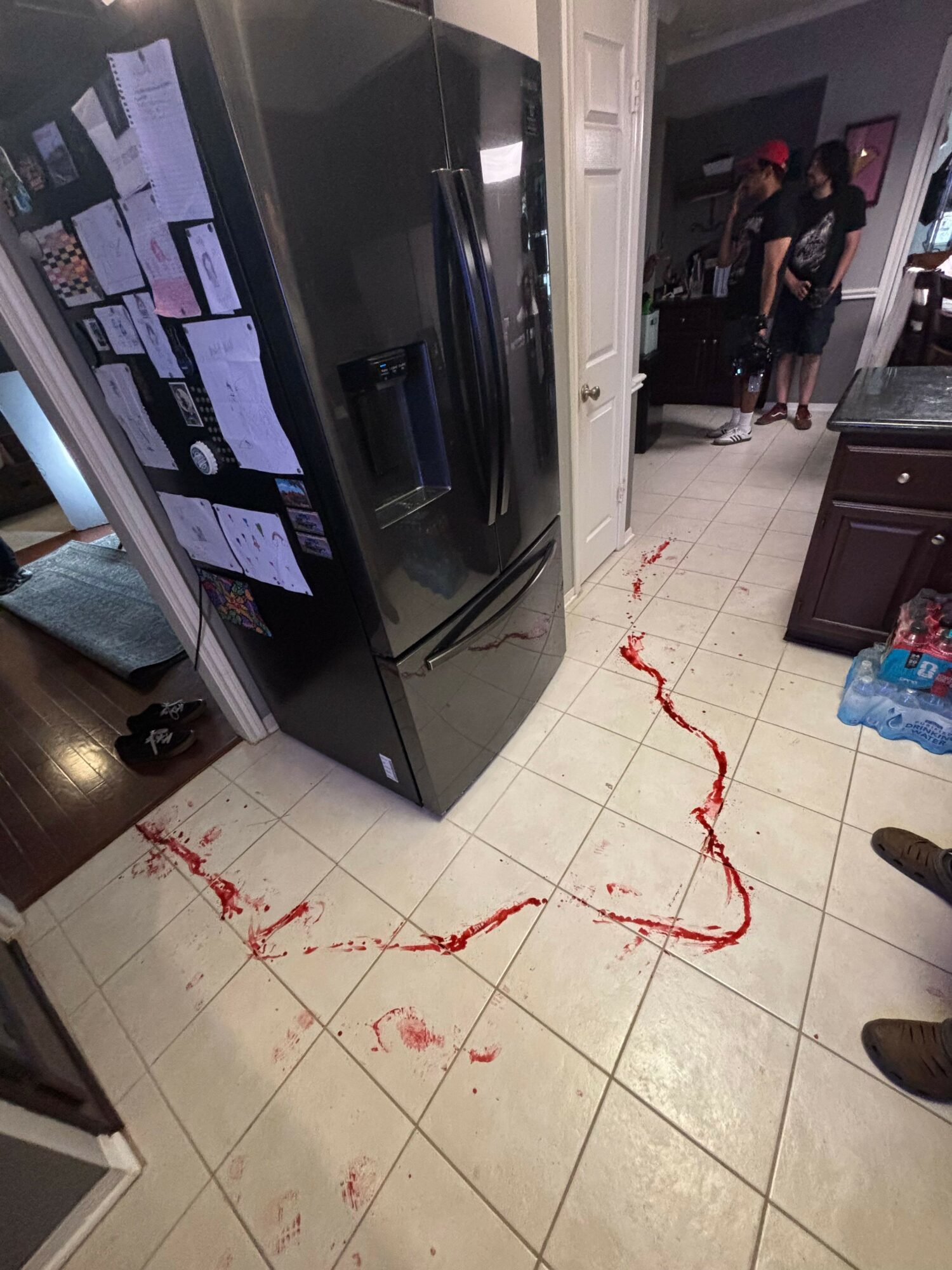 Floor with red string or tape, scattered papers, and a black appliance in a room with tiled floor and furniture.