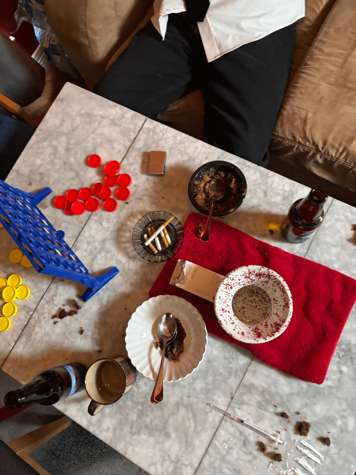Part of a table with snacks, drinks, and a red napkin, with a person sitting nearby. The table has scattered crumbs and items.