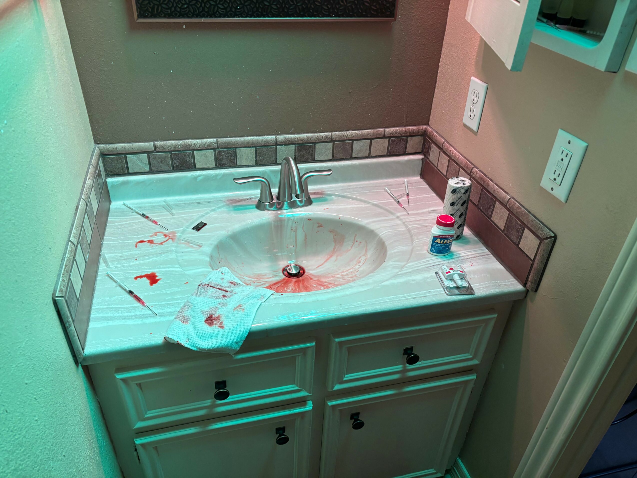 Bathroom sink with items on the countertop, including a toothbrush, toothpaste, and a container, with a tiled backsplash and wall outlets.