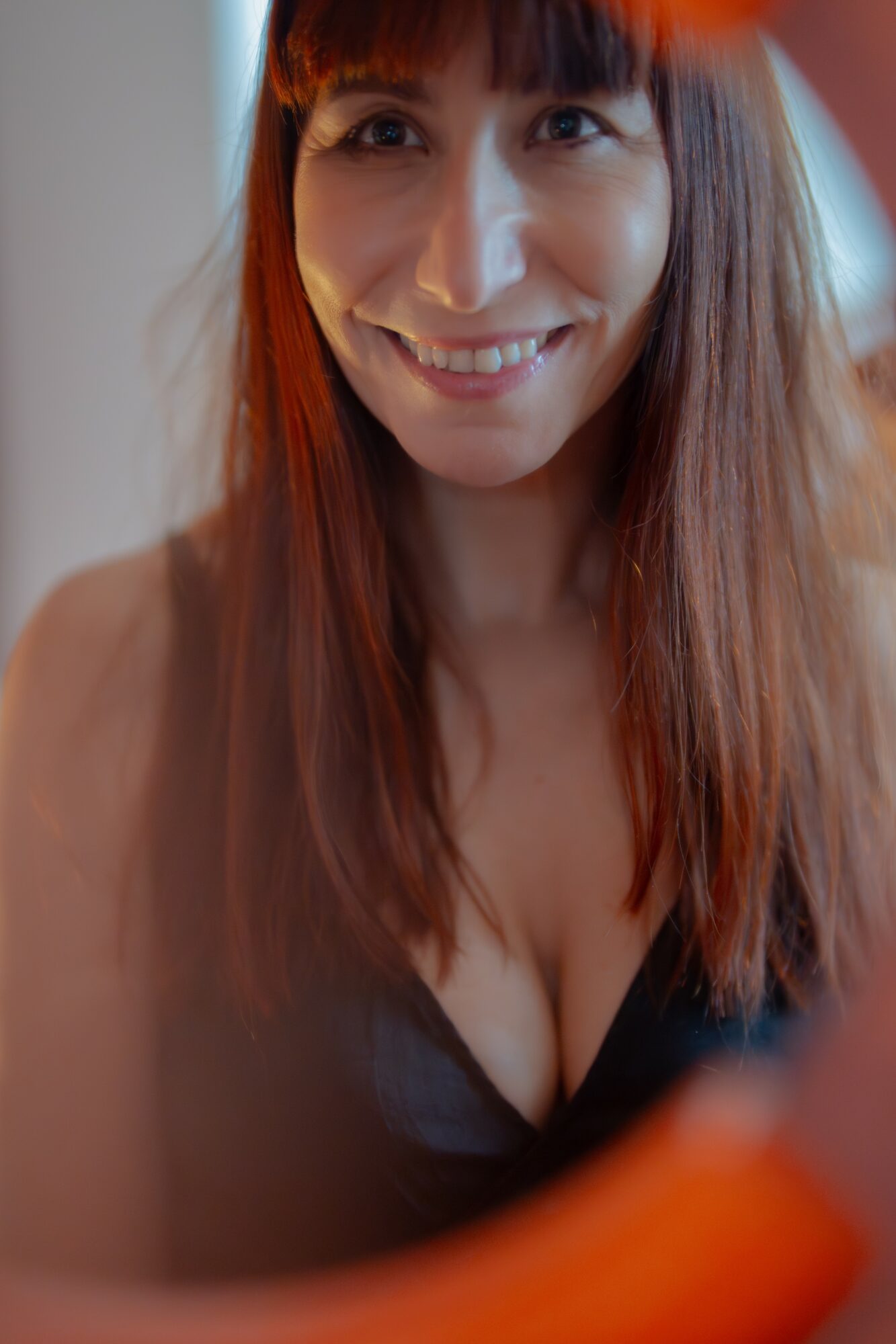 Smiling woman with long brown hair looking at camera, indoors, with soft lighting.