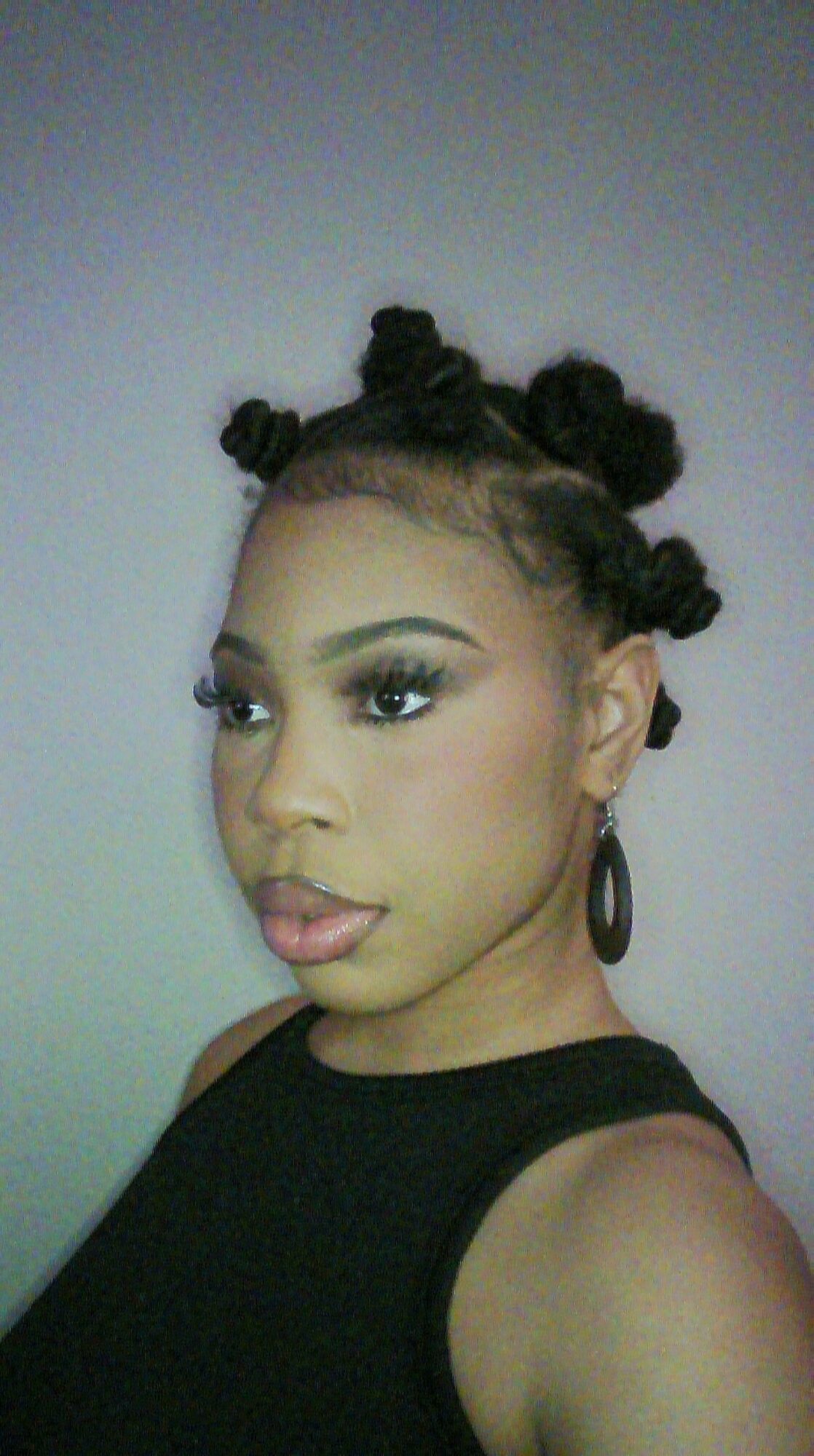 Young woman with styled hair, wearing a black sleeveless top, looking sideways, against a plain background.