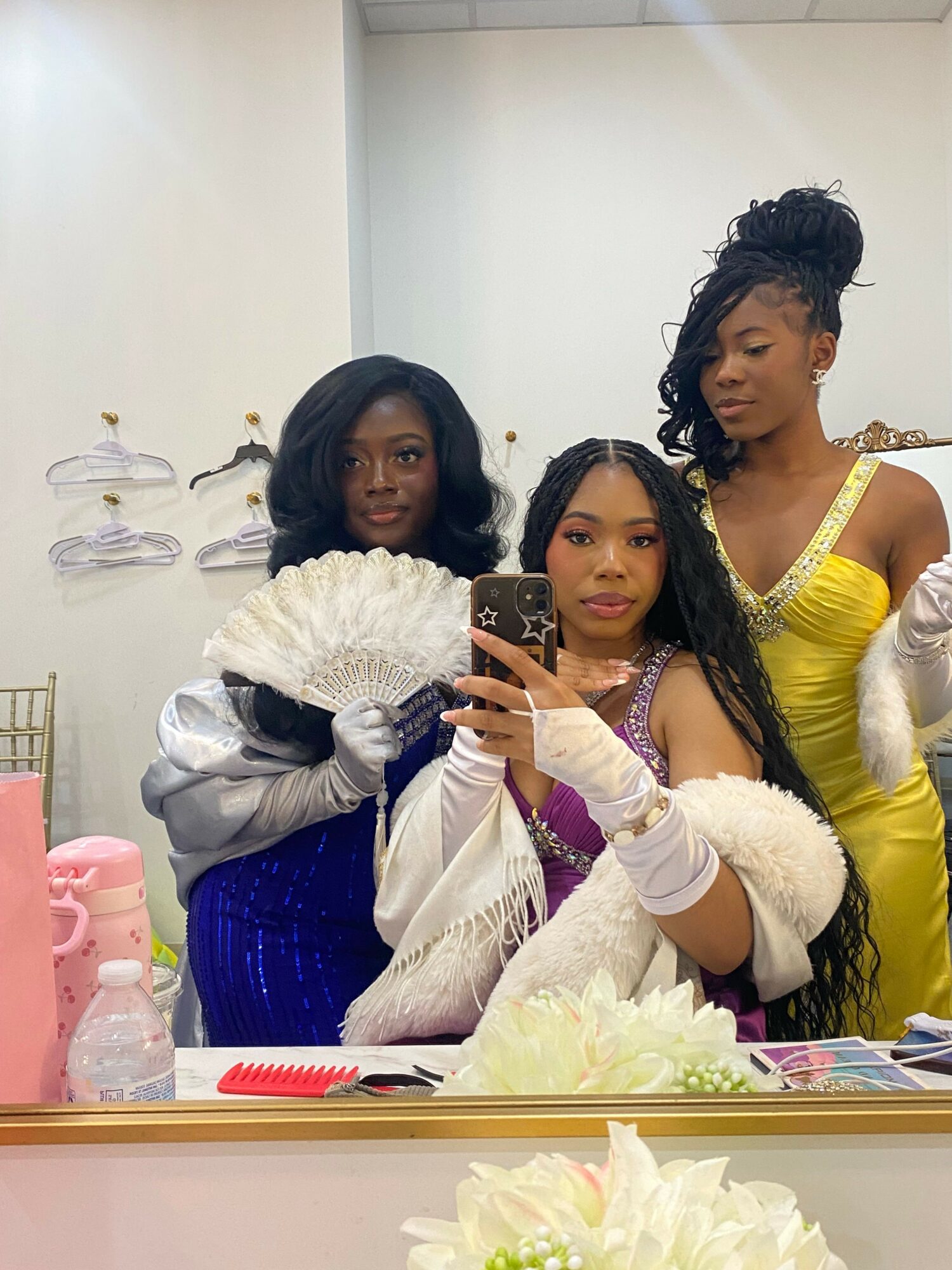 Three women in colorful costumes taking a selfie in a room with white flowers on the table.