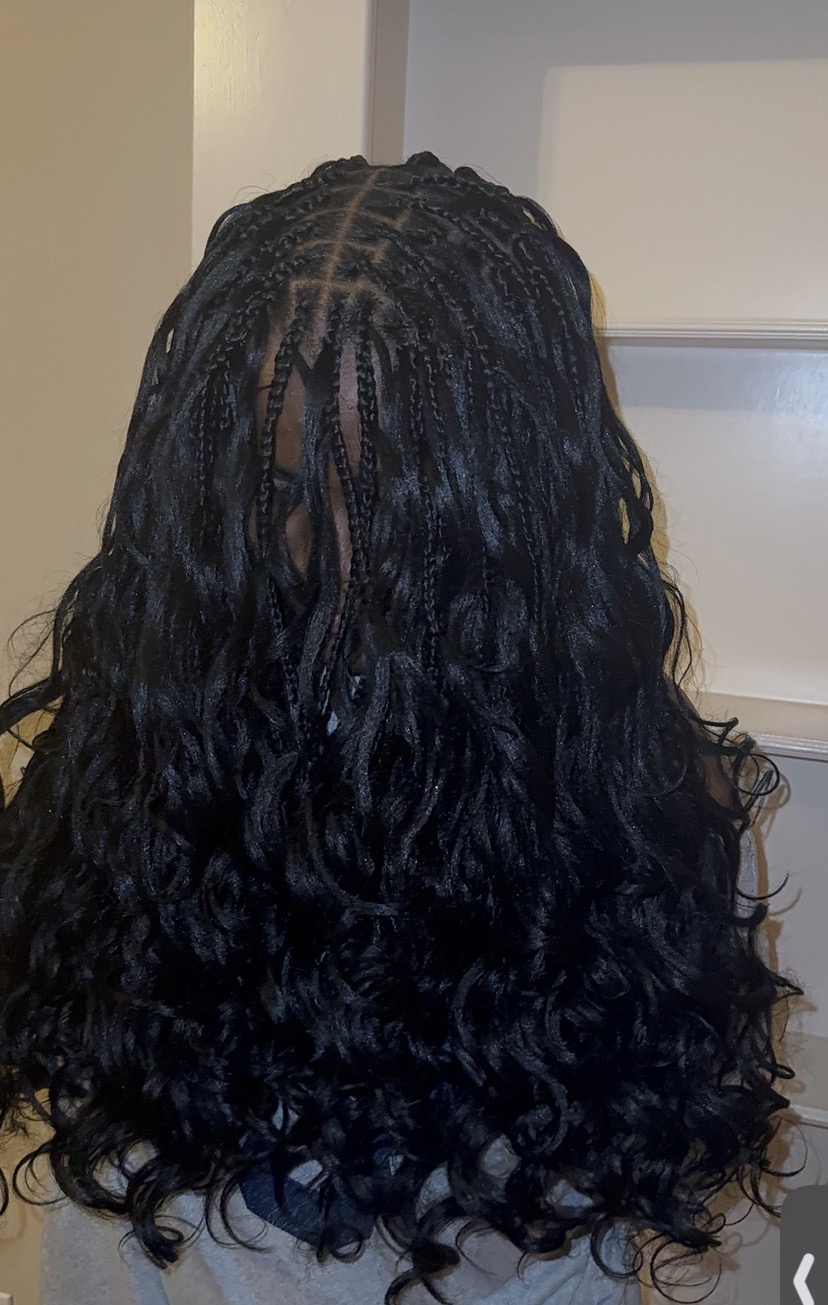 Person with long, curly, black hair viewed from behind, indoors, with a white wall and window in the background.