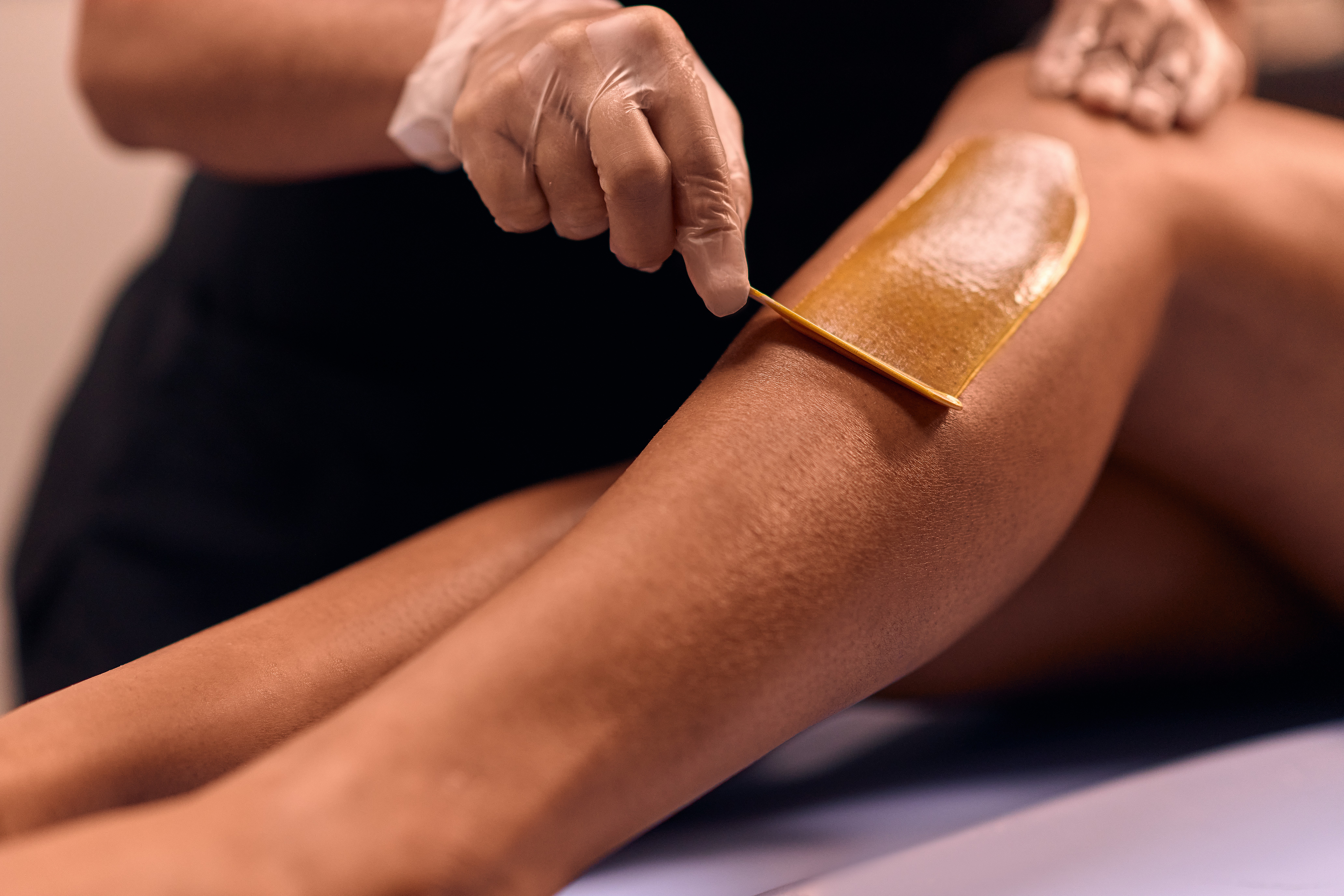 Person applying wax to a person's leg for hair removal, with a wooden spatula, close-up view.