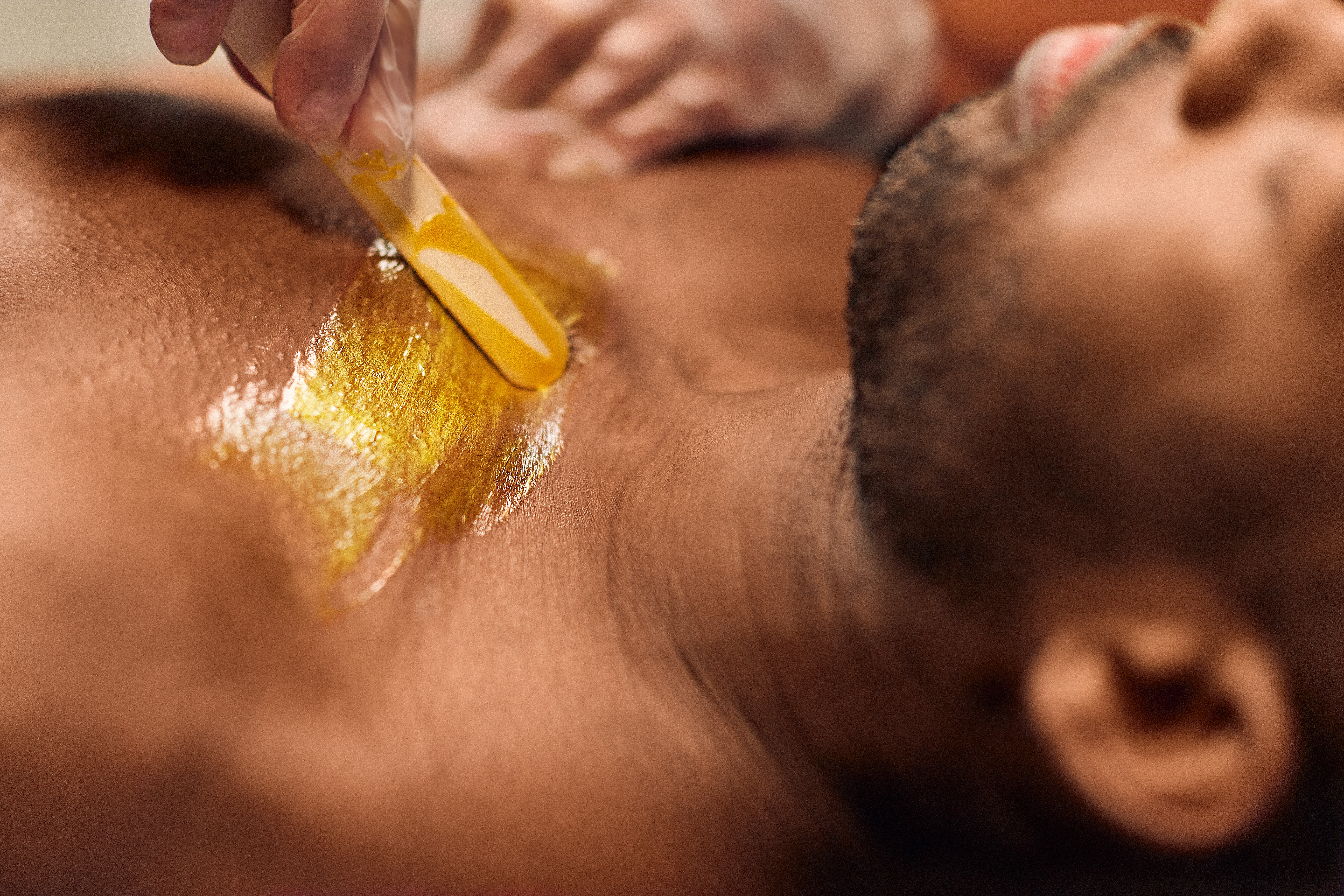 Person receiving a gold-colored treatment on their chest, lying down with a relaxed expression, close-up view.