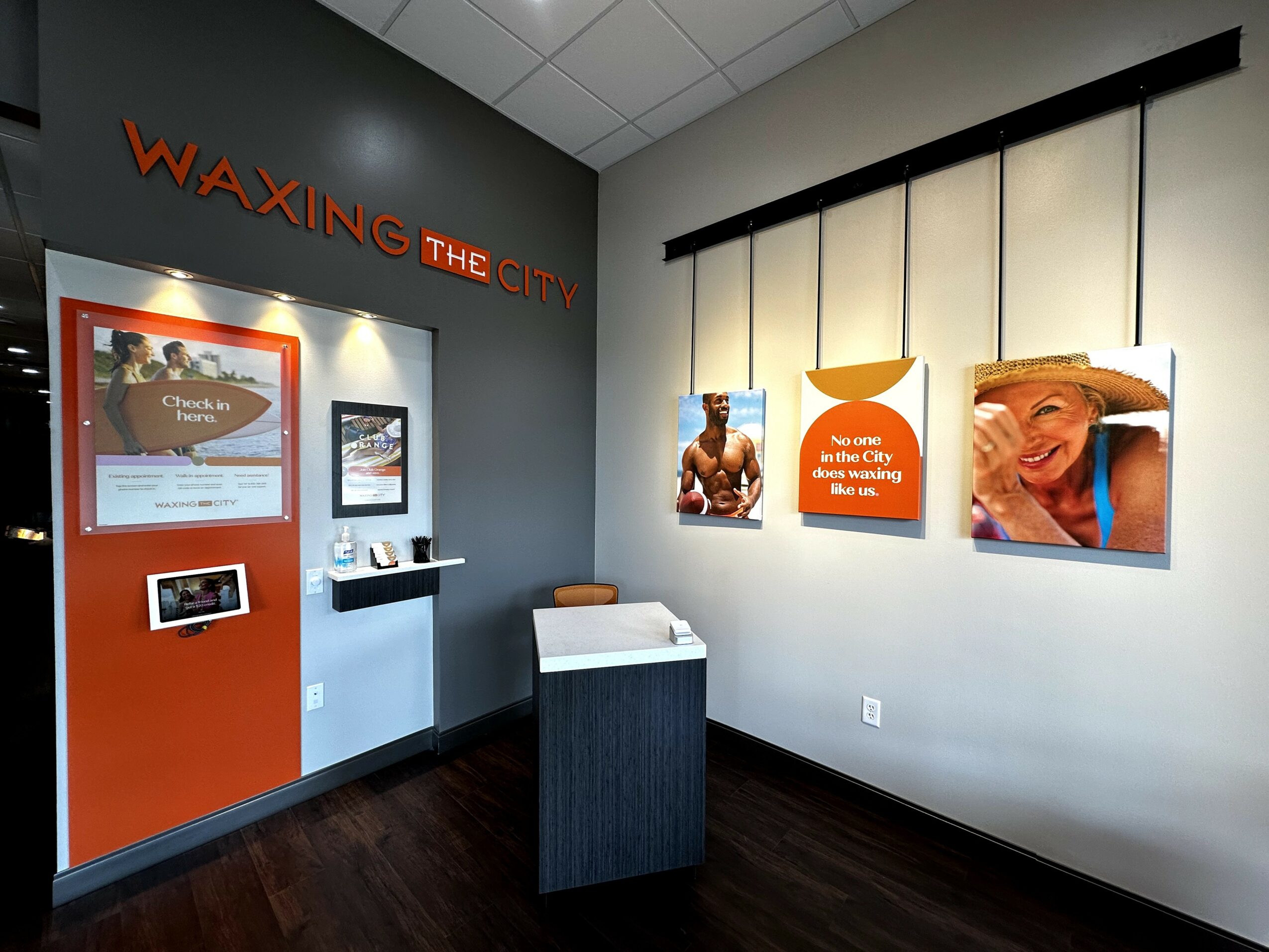 Exhibit with photos and text about Waxing the City, a waxing salon, on a gray wall with a display case and a small table.