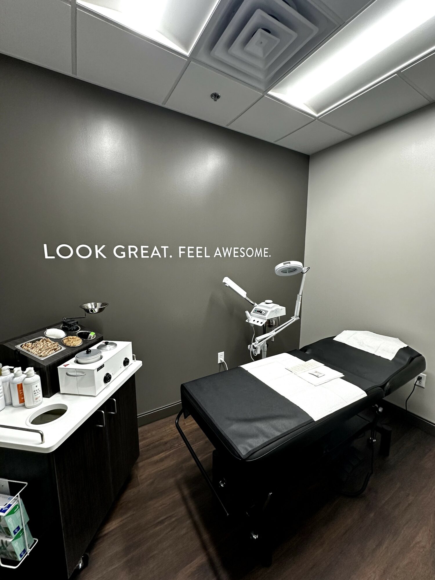 Medical examination room with a bed, a wall with motivational text, and a cart with supplies.