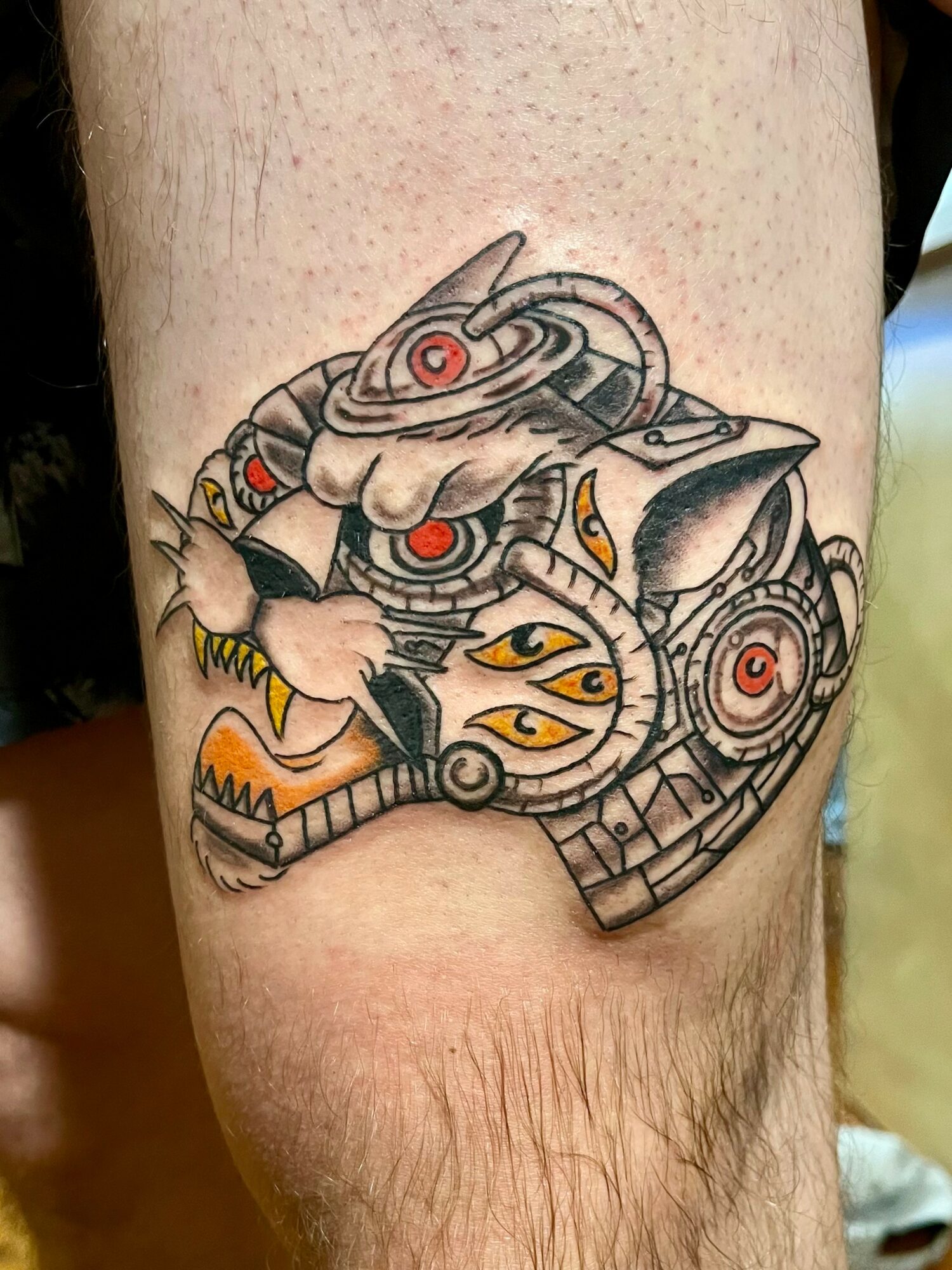 Tattoo of a robotic tiger head with mechanical details and red circular eyes, on a person's skin.