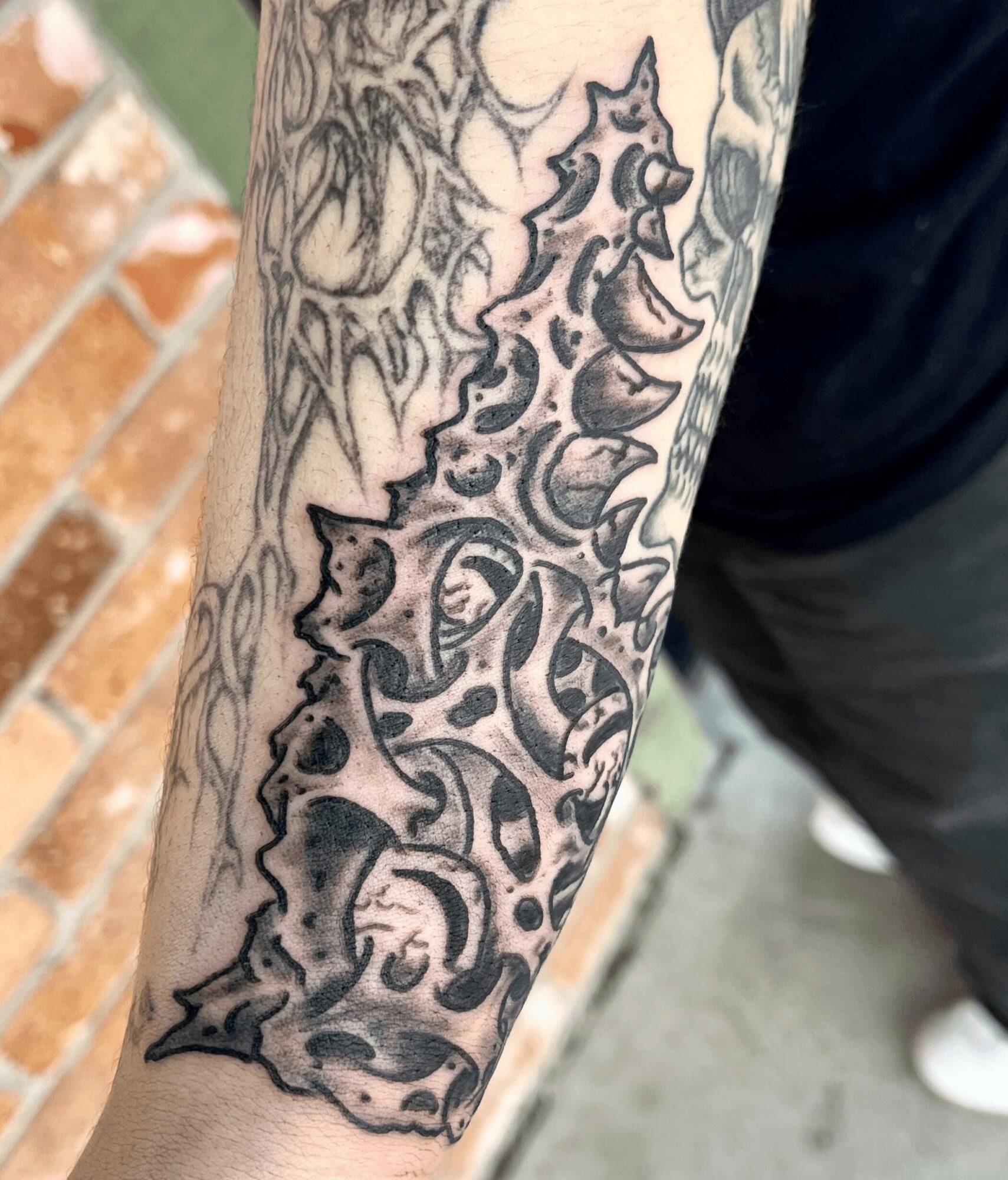 Tattoo of a stylized, abstract design with dark shading on a person's forearm.
