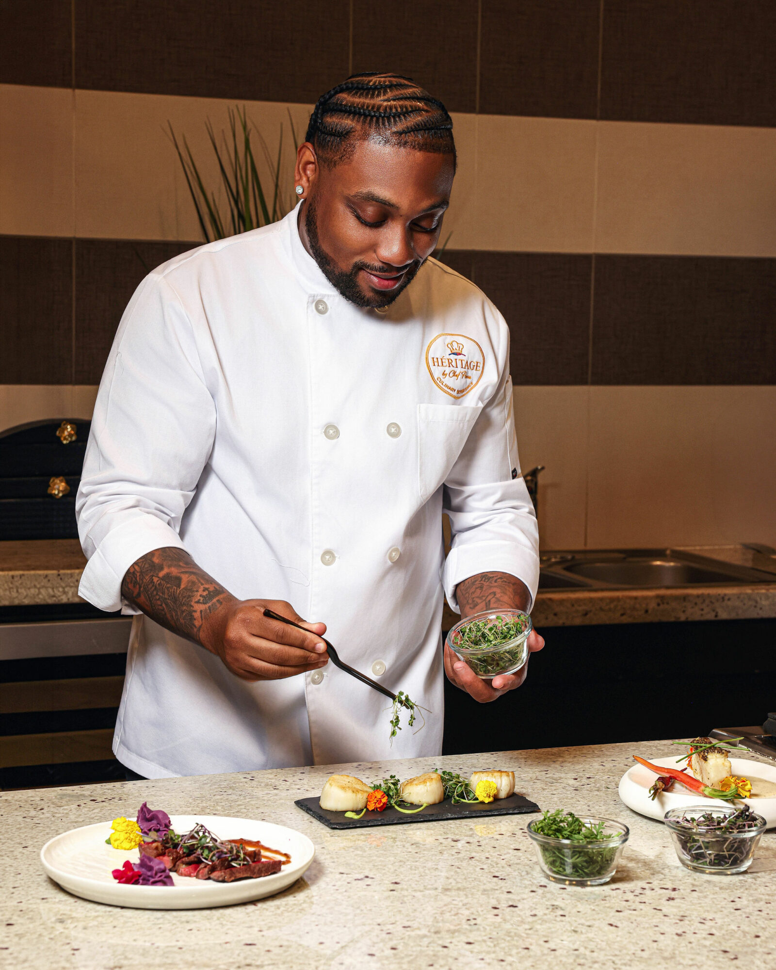 Chef in white uniform preparing food with herbs and garnishes on a kitchen counter.