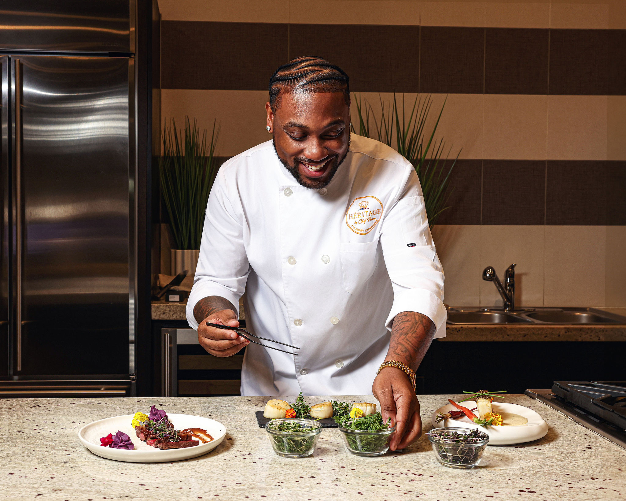 Chef smiling, preparing food with plates and ingredients on a kitchen counter.
