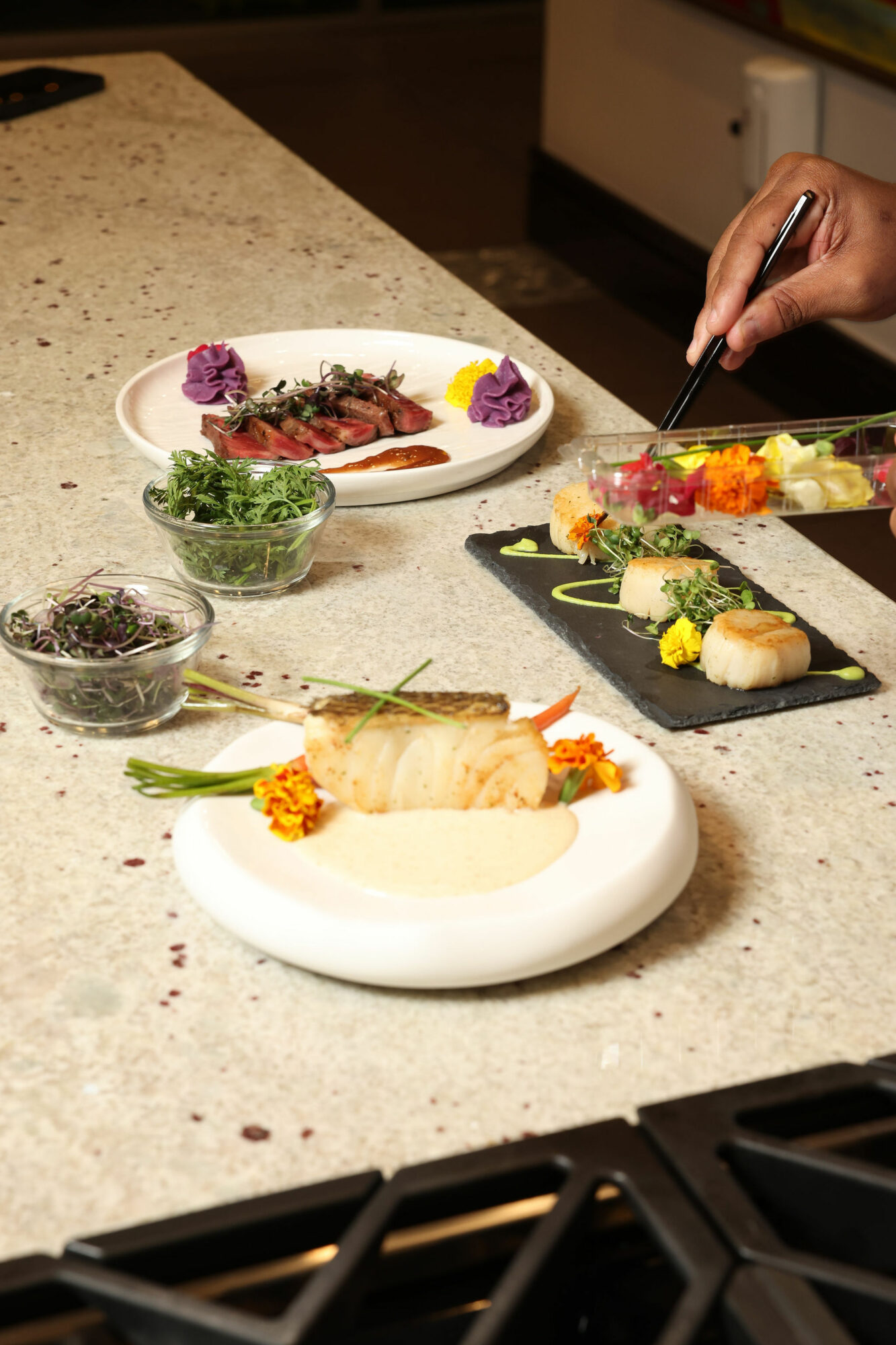 Person preparing sushi with various ingredients on a kitchen counter, including a plate with sushi rolls and garnishes.