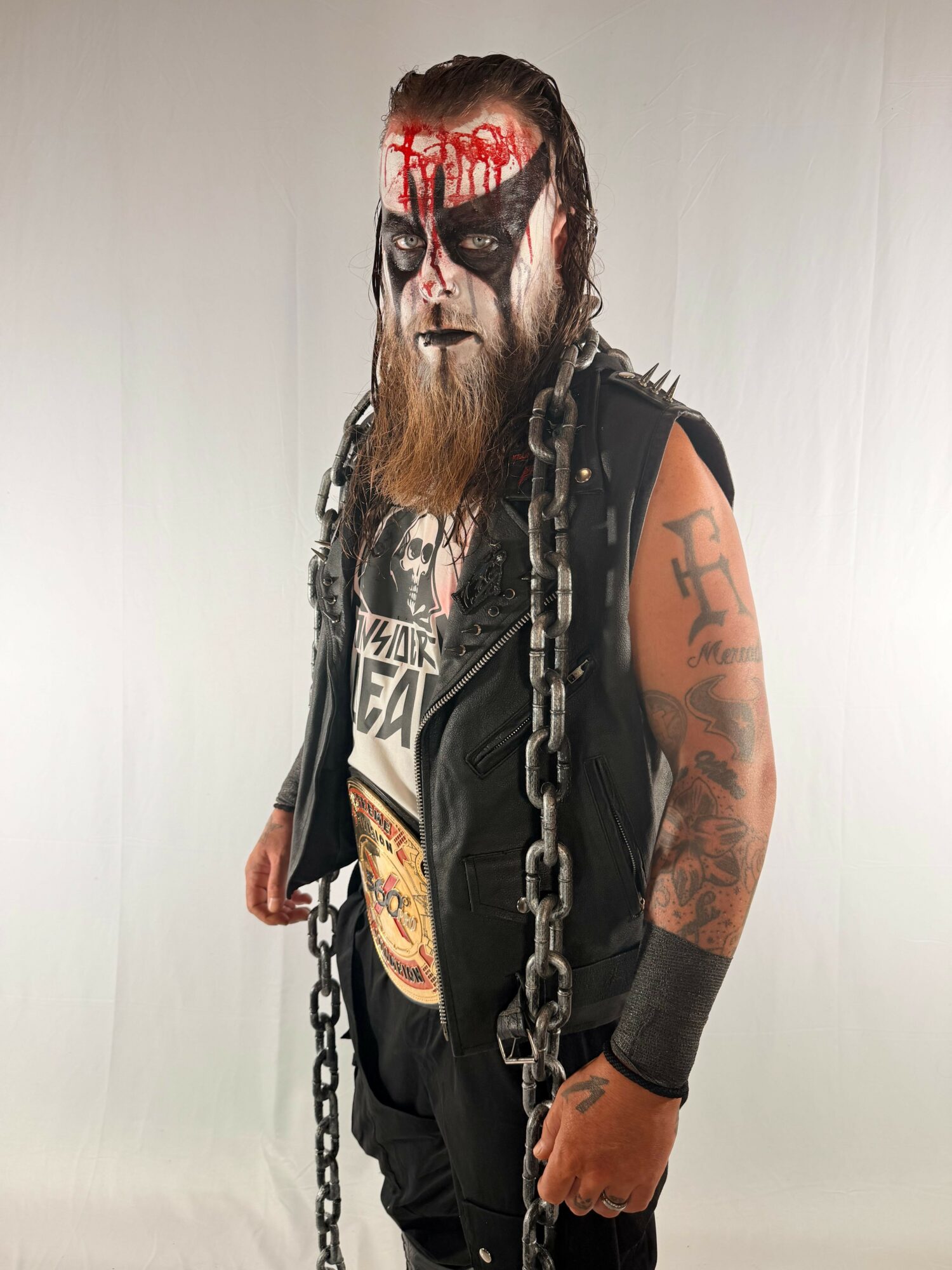 Person with face paint, tattoos, and chains, standing sideways against a plain background.