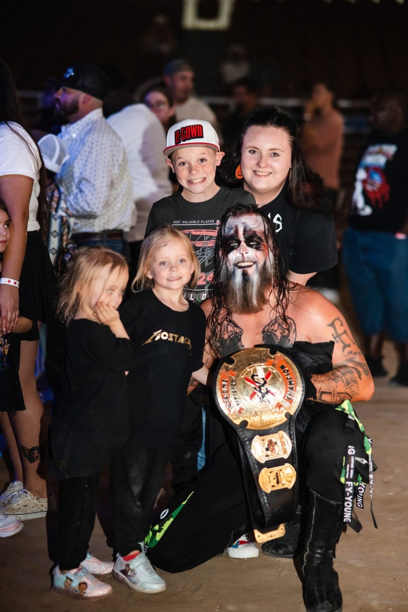 Group of children and a woman with face paint, some smiling, in a dimly lit indoor setting.