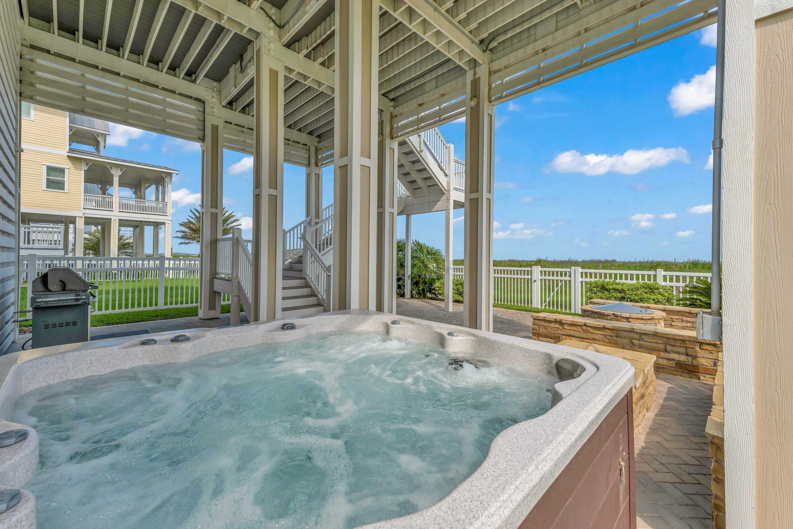 Hot tub with bubbling water on a screened porch overlooking a grassy yard and blue sky with clouds.