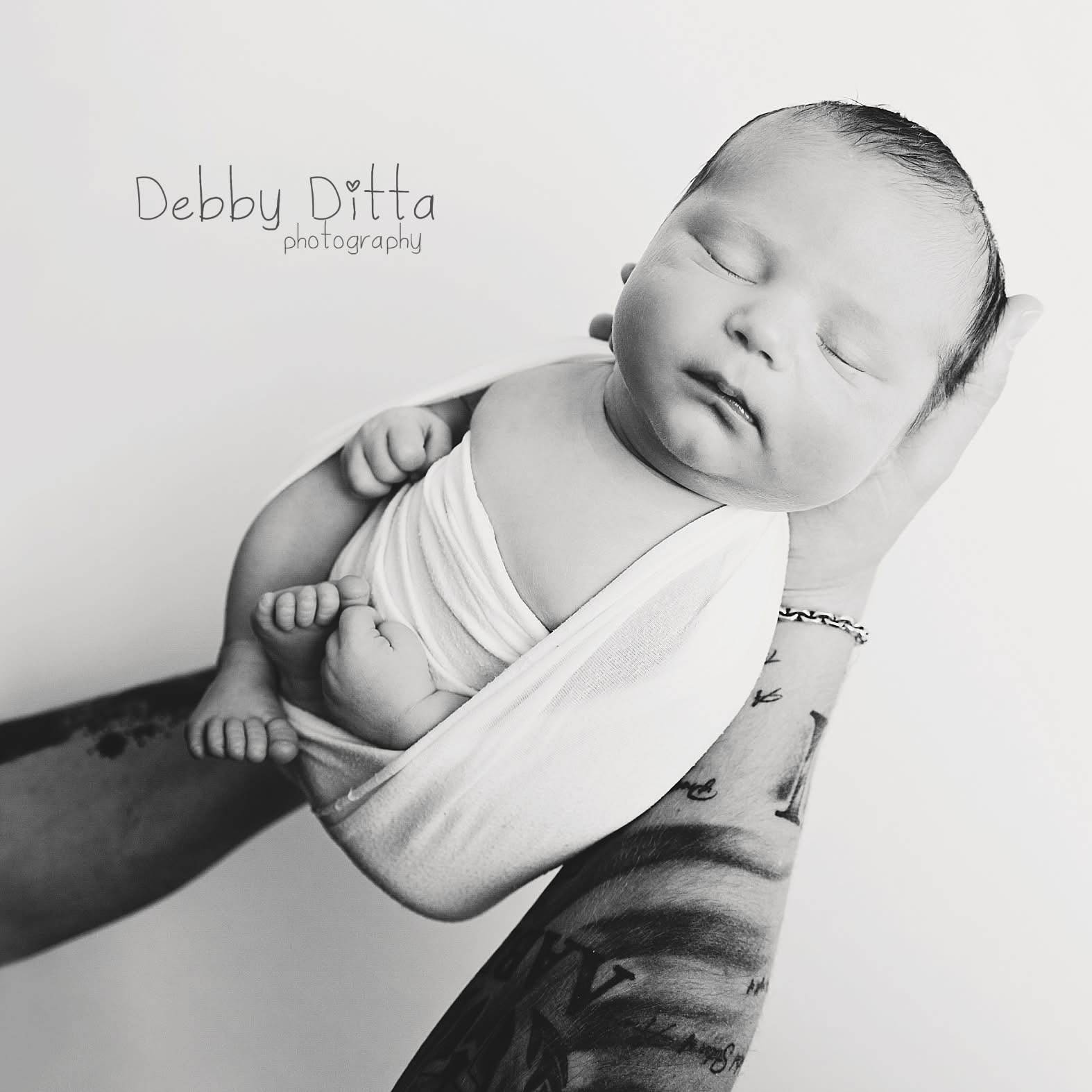Newborn baby wrapped in cloth, sleeping in an adult's hand, black and white photo, gentle expression, soft lighting.