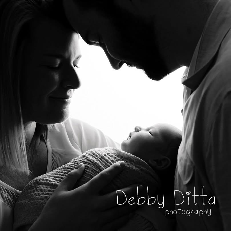 Silhouette of a family with a baby, parents smiling and looking at the infant, in black and white, with text 'Debby Ditta photography'.