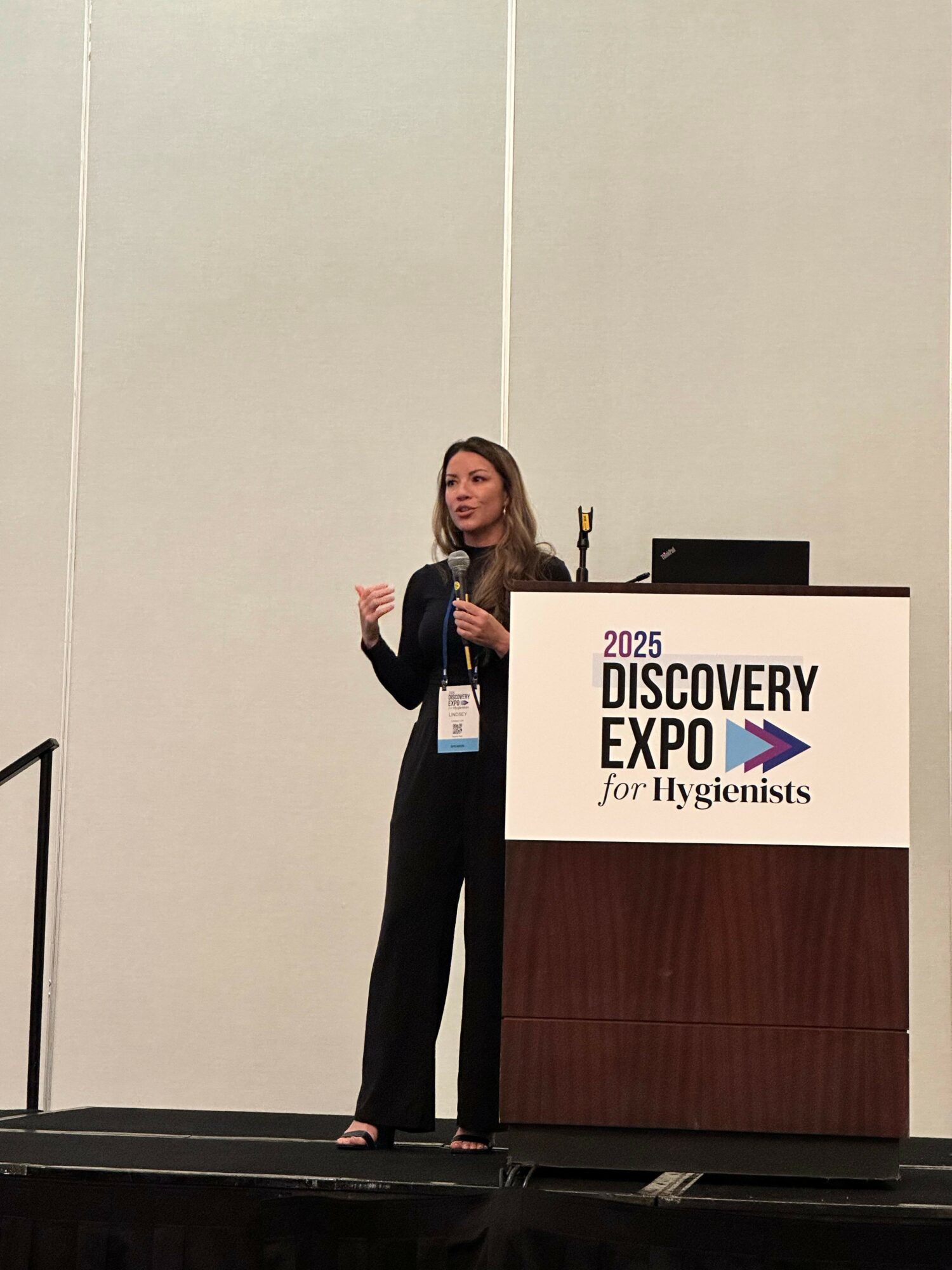 Woman speaking at a podium during a conference, with a sign reading 'Discovery Expo' behind her.