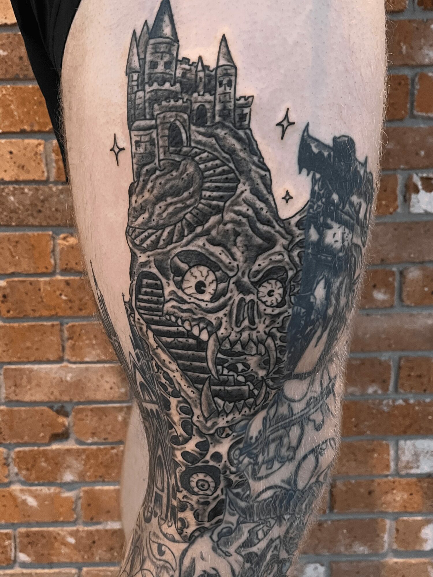 Tattoo of a skull with a castle on top, surrounded by dark, swirling designs and a flying bird, on a person's leg.
